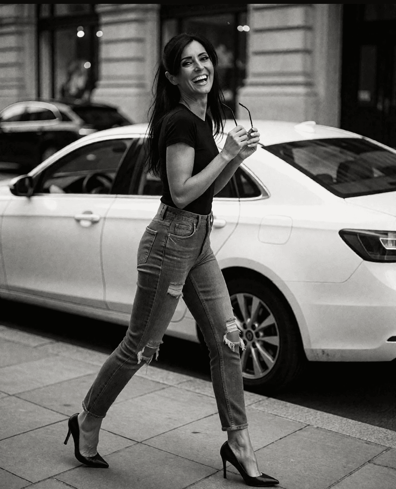 Silvia Rizzo walking beside a car in a black T-shirt, ripped jeans, and high heels.