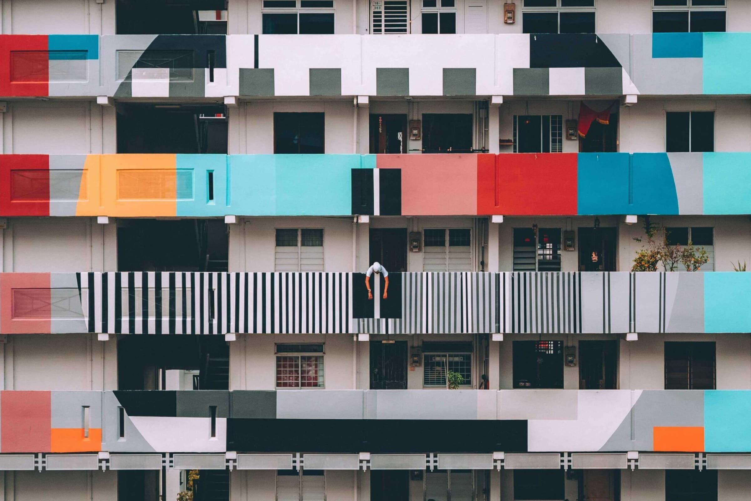 A man leaning over the balcony of a colourfully painted high rise block