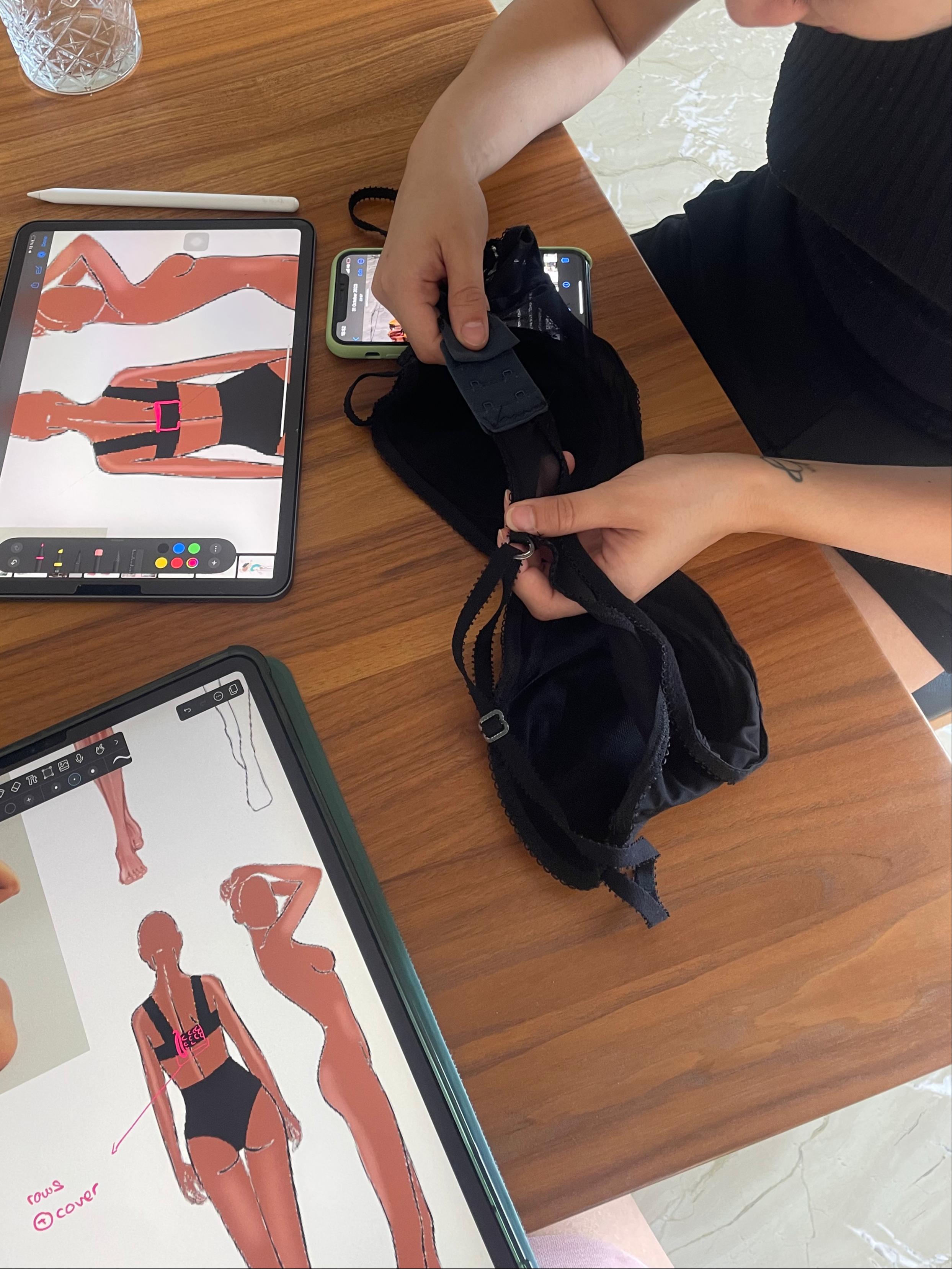 Person at table reviewing a black bra prototype with sketches and a tablet nearby.