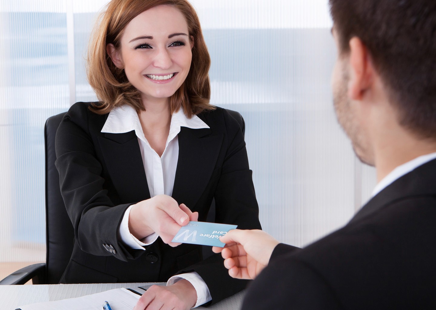 Una datrice sorridente, porge una carta welfare ad un dipendente compiaciuto del gesto