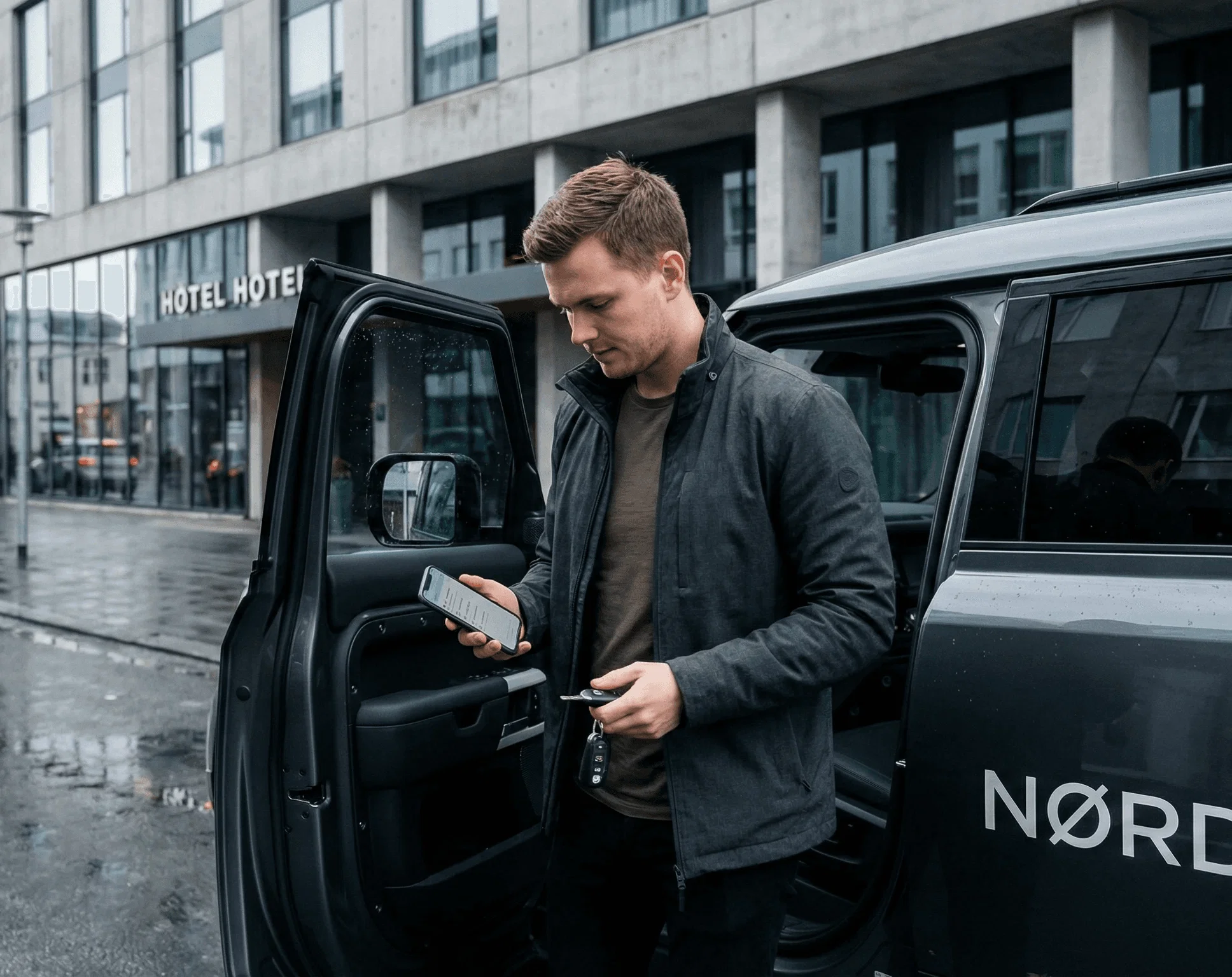 Man looking at a phone while standing next to a car door.