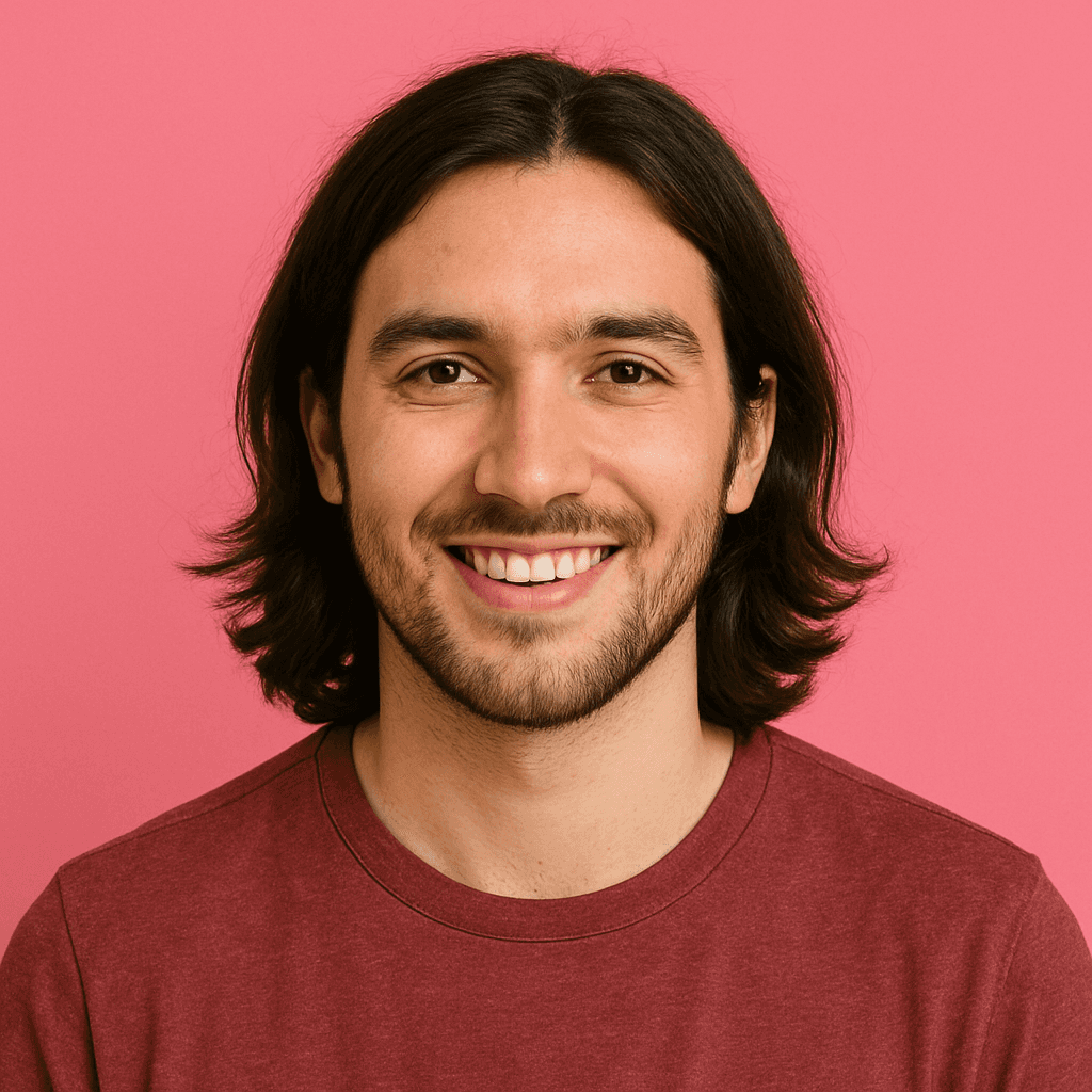 A smiling man with long hair and a beard in a maroon shirt stands against a pink background, conveying a warm and friendly tone.
