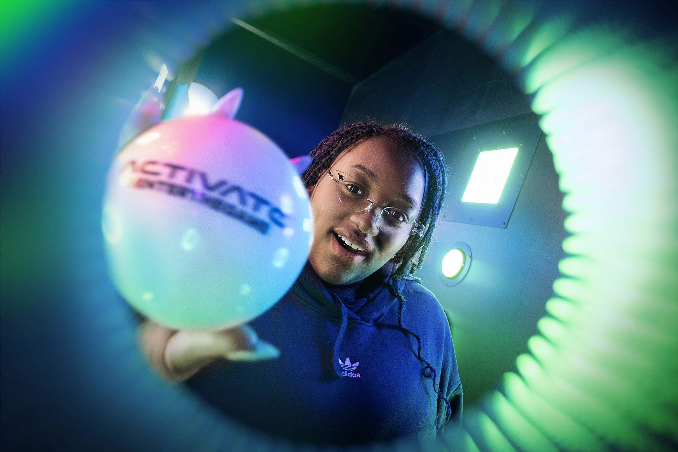 A young woman holds a glowing Activate Entertainment ball inside a vibrant, neon-lit tunnel.