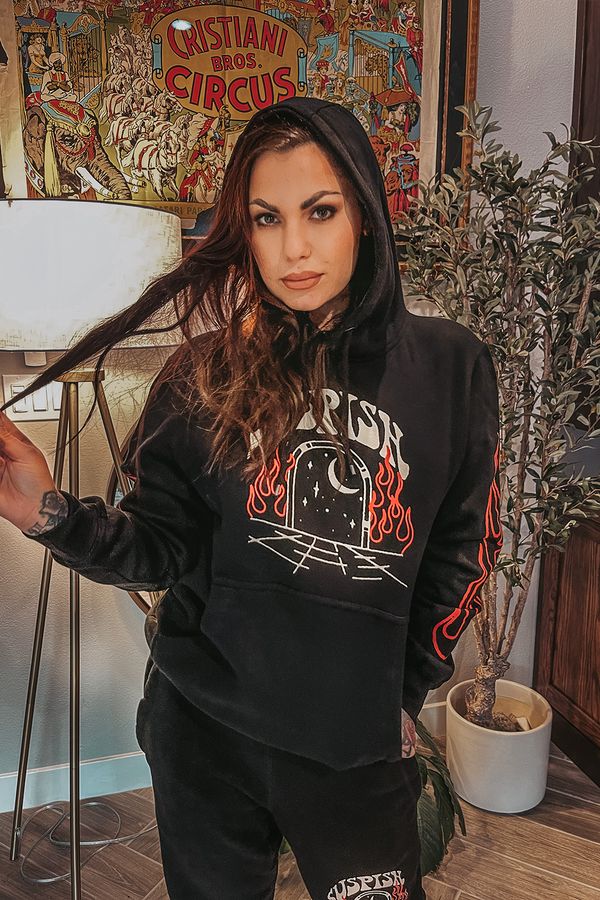 A young woman wearing a black hoodie stands indoors, holding a plant pot beside a decorative wall.