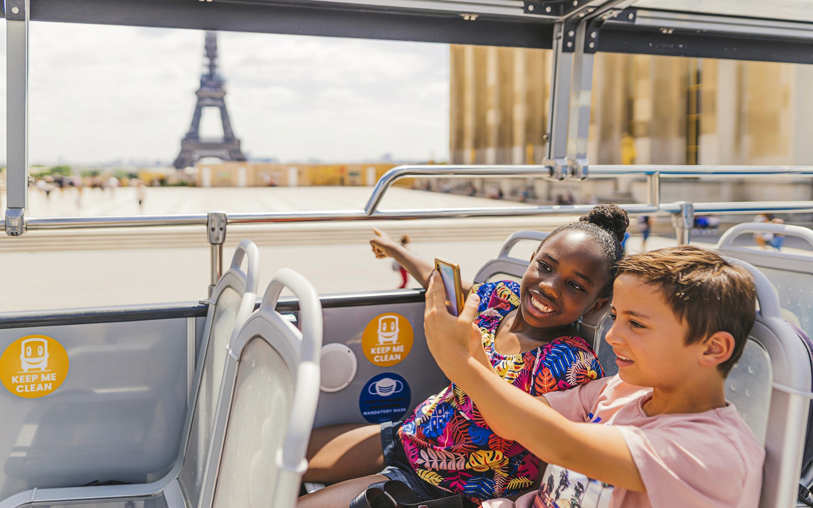 Children on a double-decker bus enjoying an audio-guided tour with the Eiffel Tower in the background.