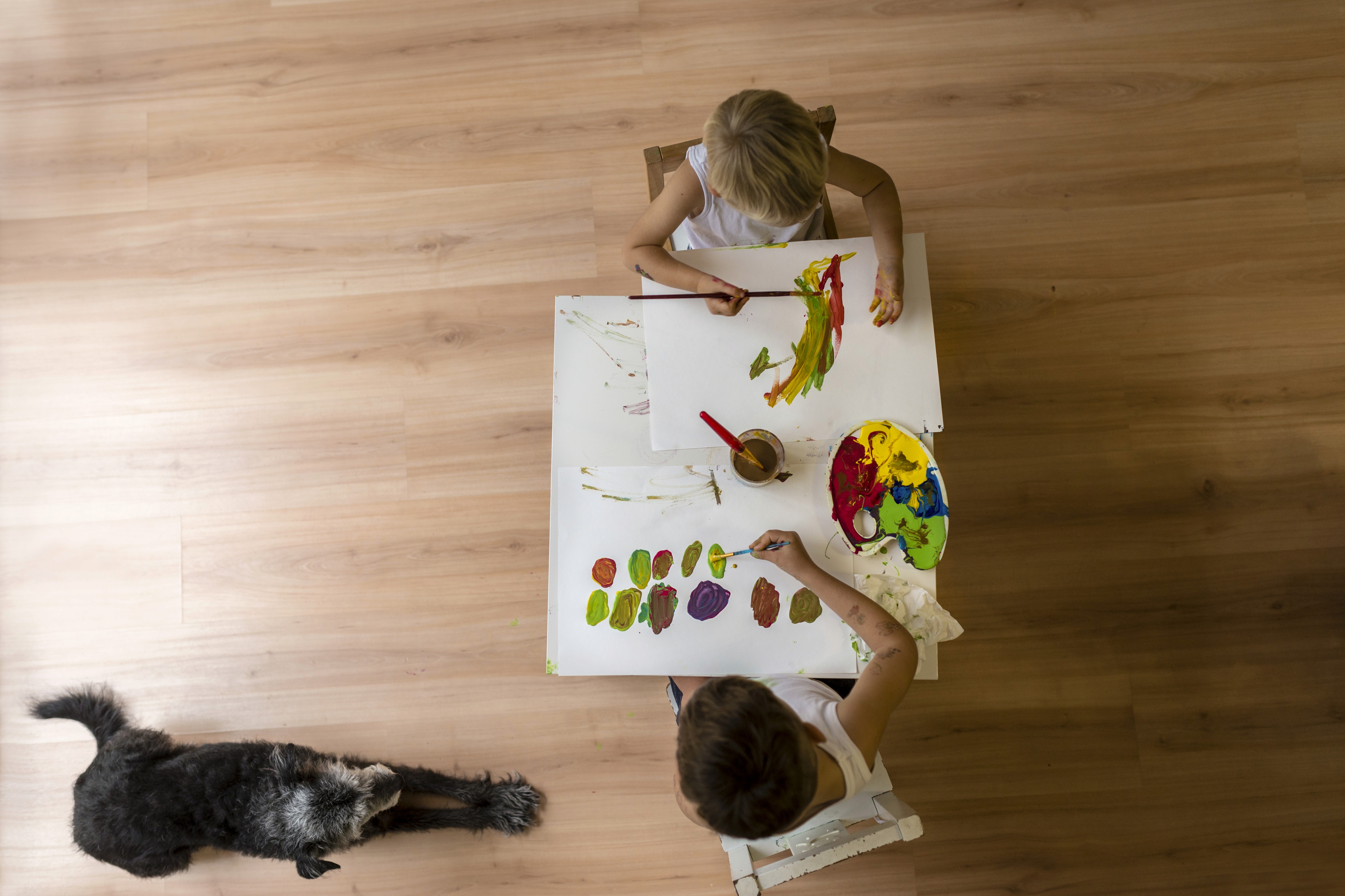 Children paint and create together at a small table on LUXO’s warm wood-look hybrid flooring, with a family dog resting nearby. The durable, stain-resistant, and easy-clean surface highlights LUXO Floors’ family- and pet-friendly design, ideal for Brisbane and Australian homes.