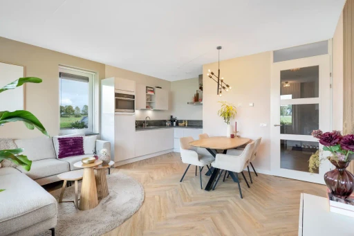 De open woonkamer met een hoekbank, een houten eettafel en zicht op de keuken.