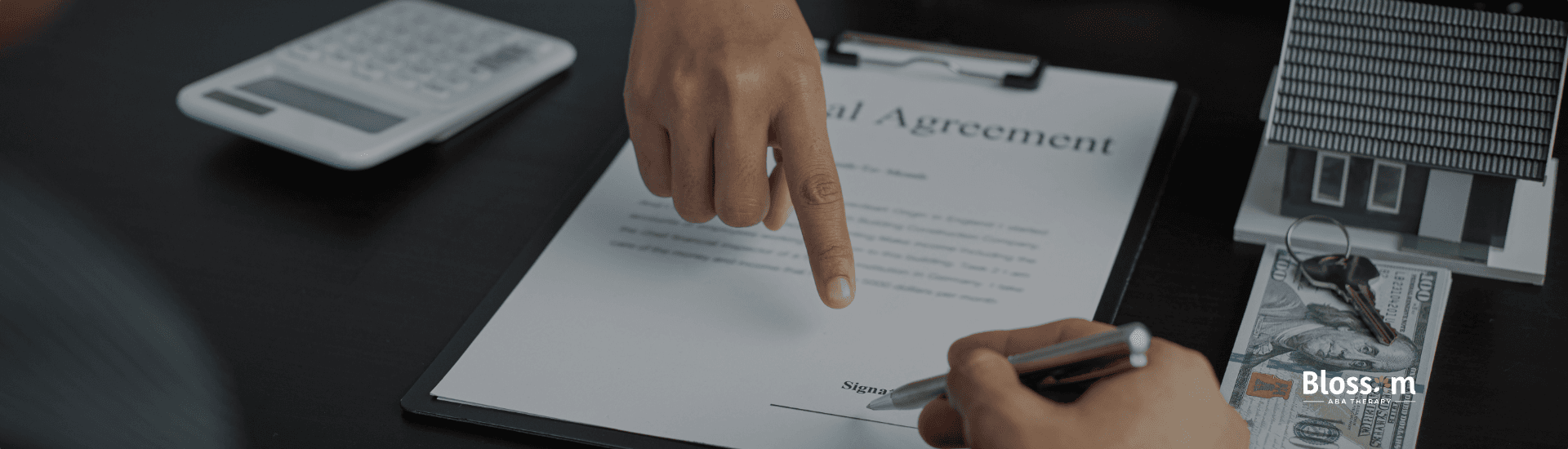 Person pointing to the signature line on an agreement form while another person signs it with a pen.