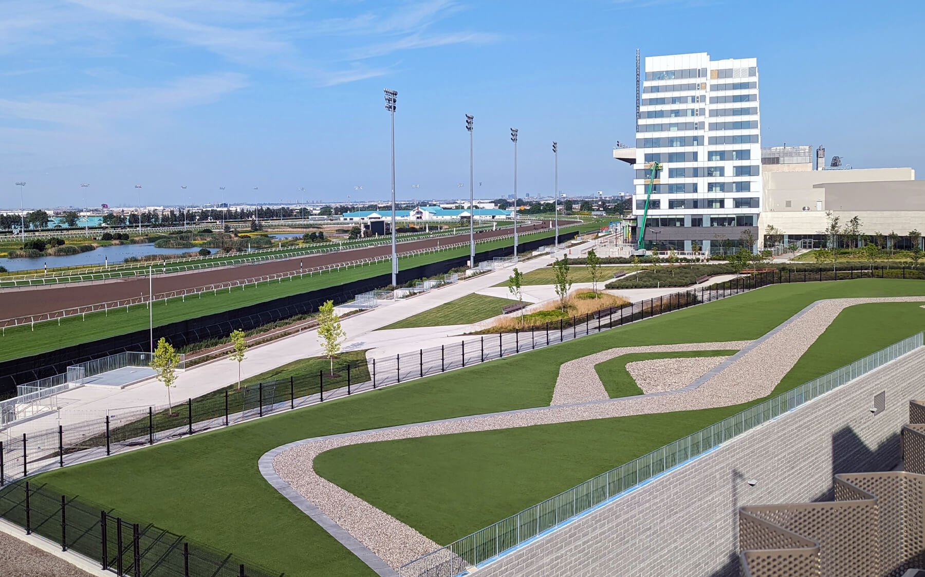 A scenic view of a horse racing track framed by vibrant greenery and a few trees against a bright sky.