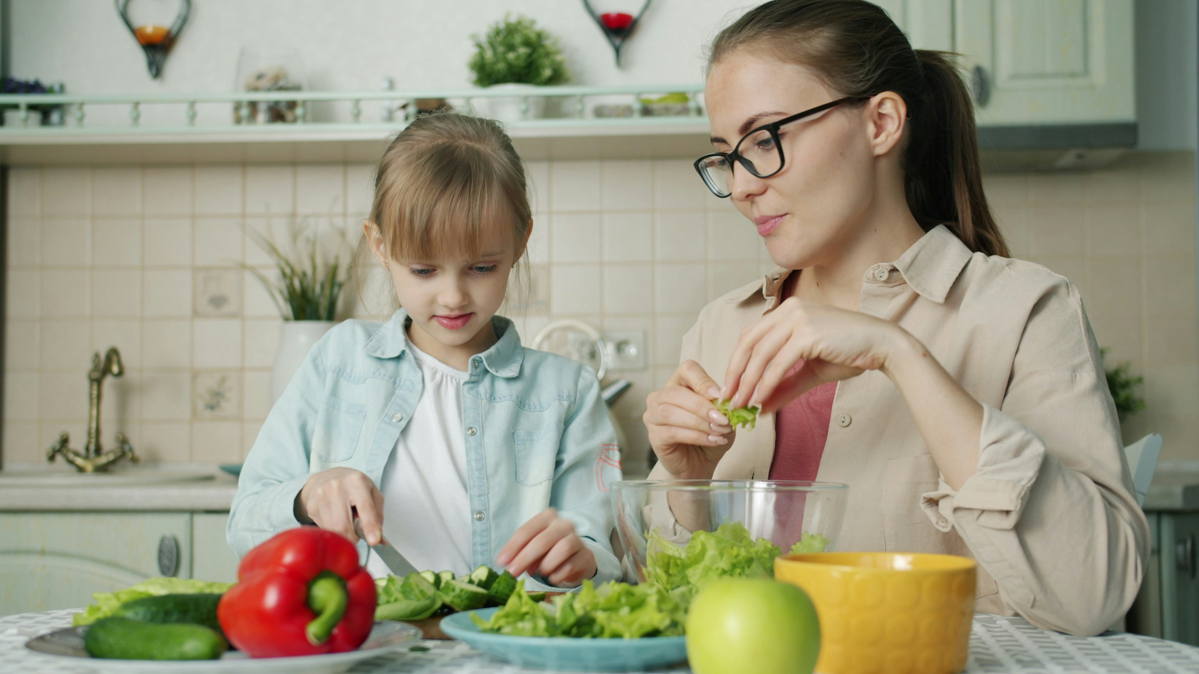 Mother and daughter preparing salad in kitchen.