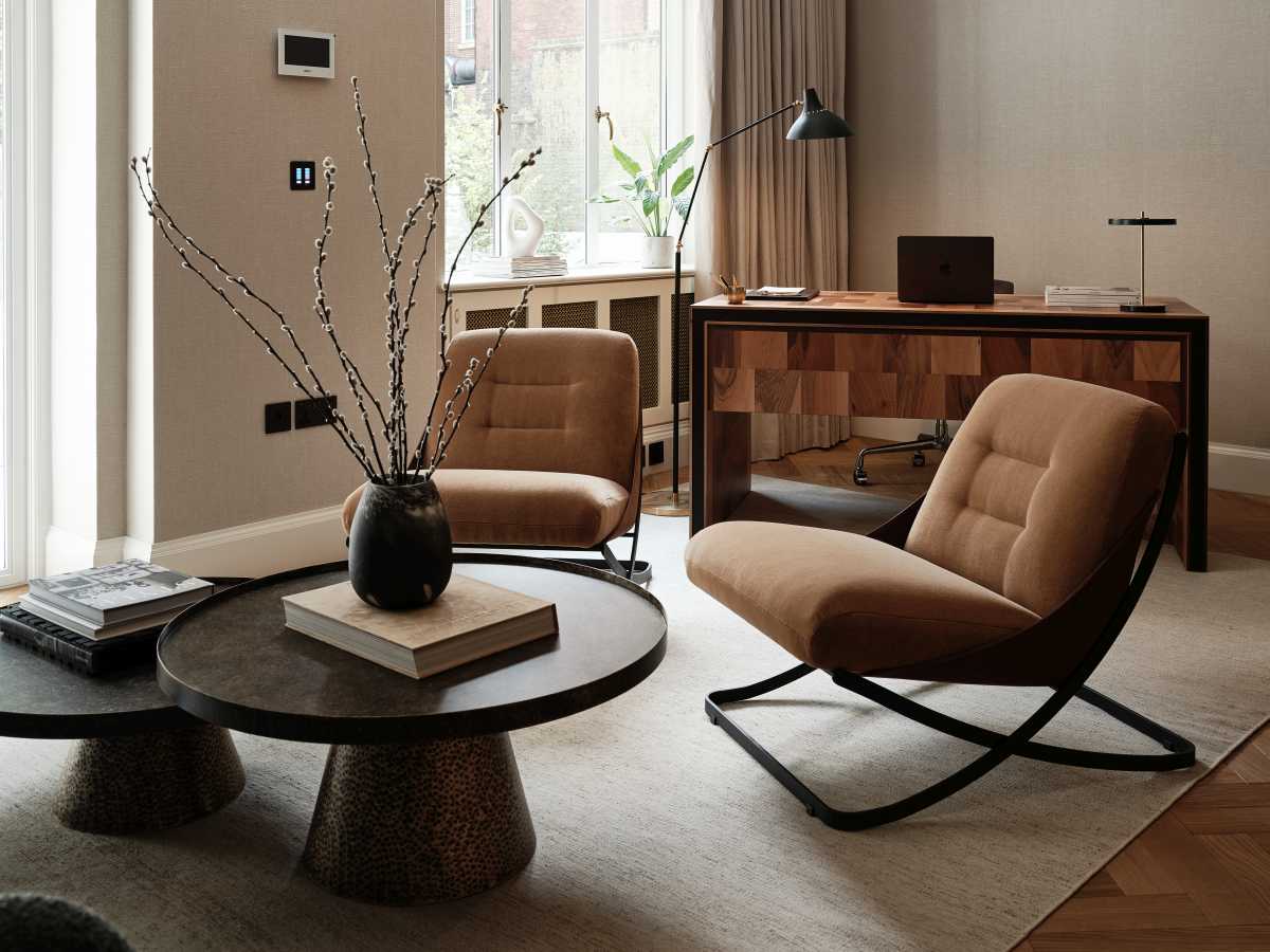 An open-plan luxury home office in London featuring low-slung, ergonomic tan leather armchairs arranged around nested dark wood coffee tables, with a sophisticated wooden executive desk positioned in the background.