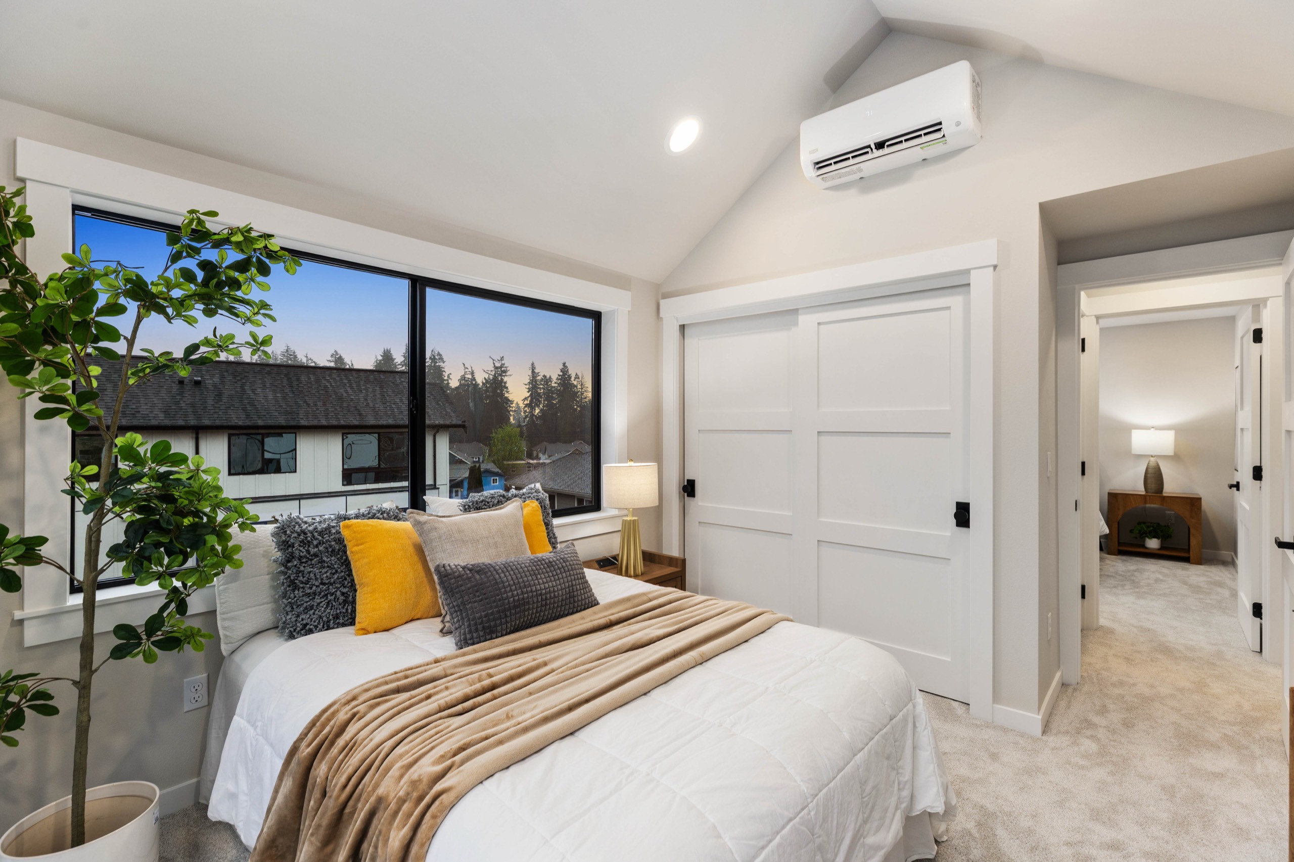Bright luxury primary bedroom with vaulted ceiling, large picture window with neighbourhood views, plush carpet, mini-split HVAC, and double closet doors