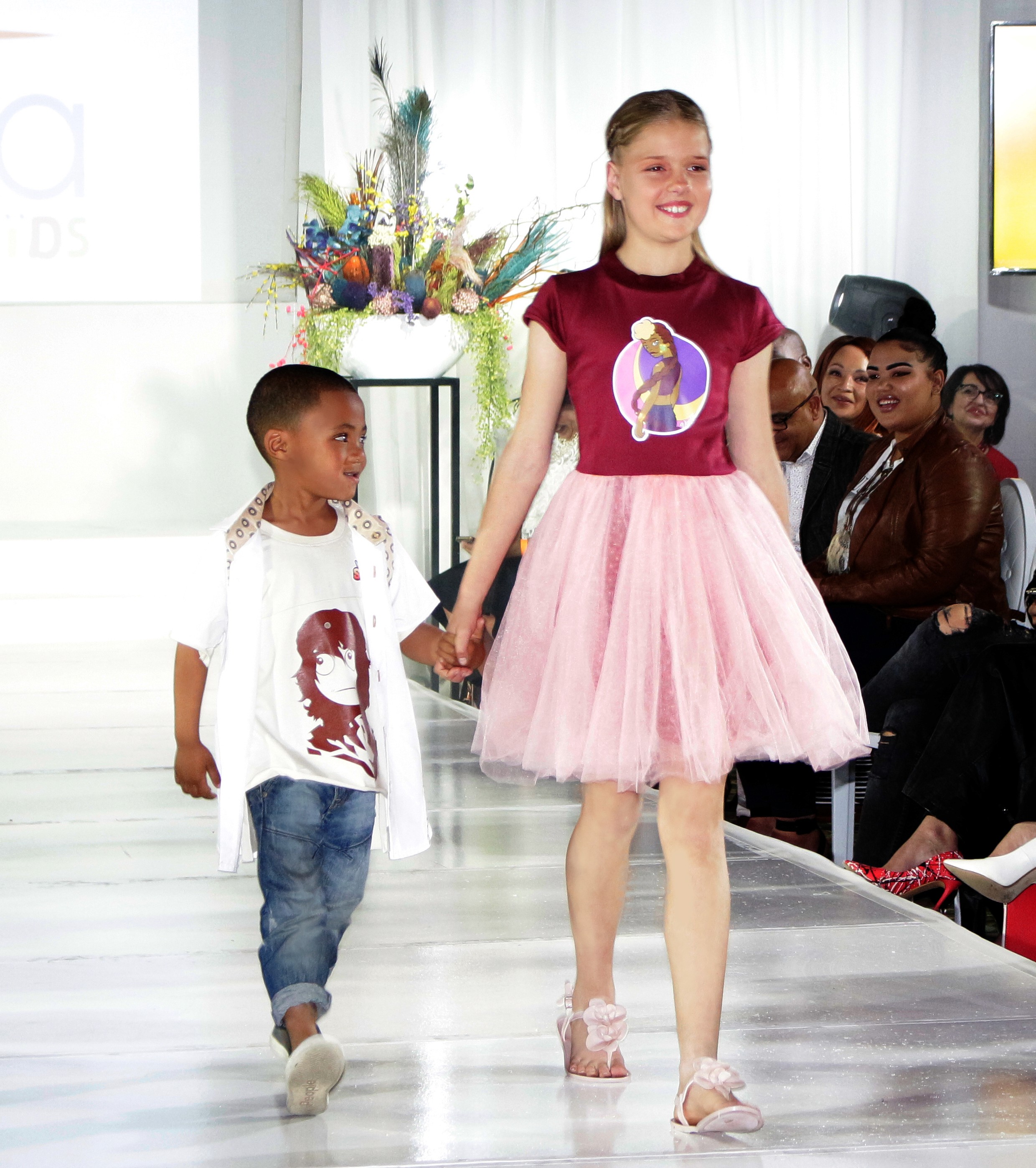 A little boy and girl walking down a catwalk hand in hand while werarin KN Studios merchandise.