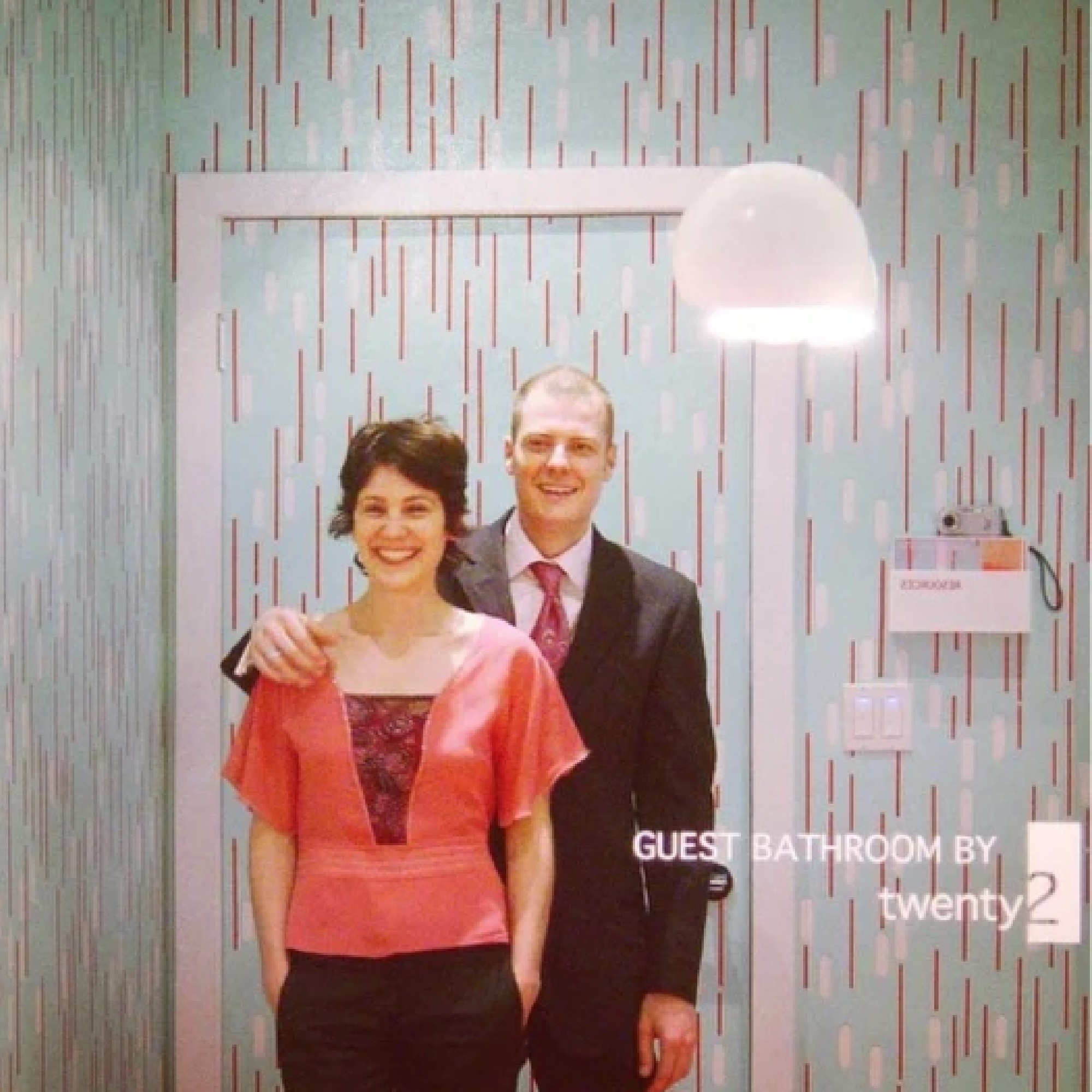 Kyra and Rob Hartnett posing in a bathroom wallpapered with their screen printed wallpaper.