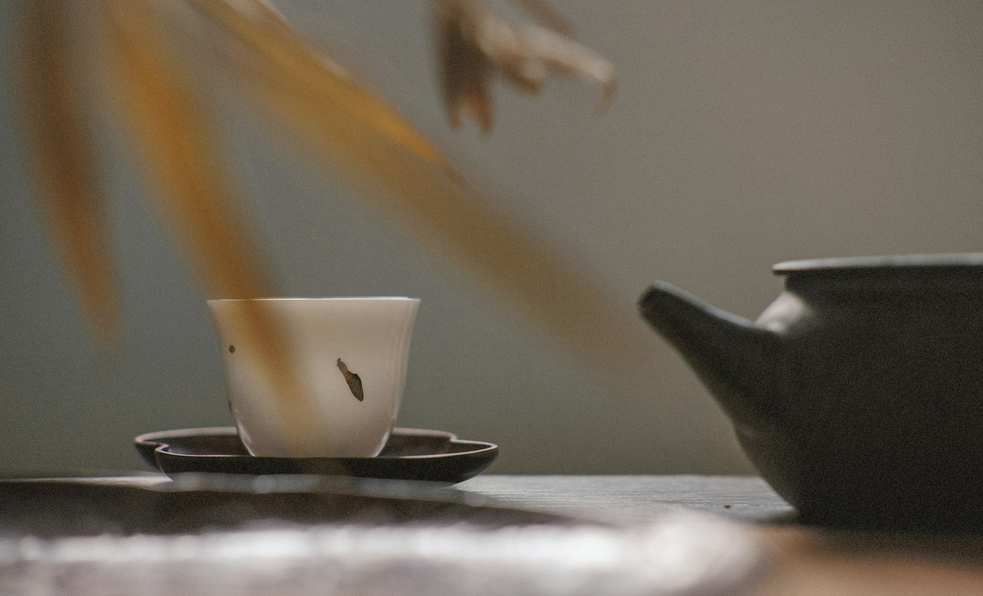 White tea cup on black saucer near black tea pot