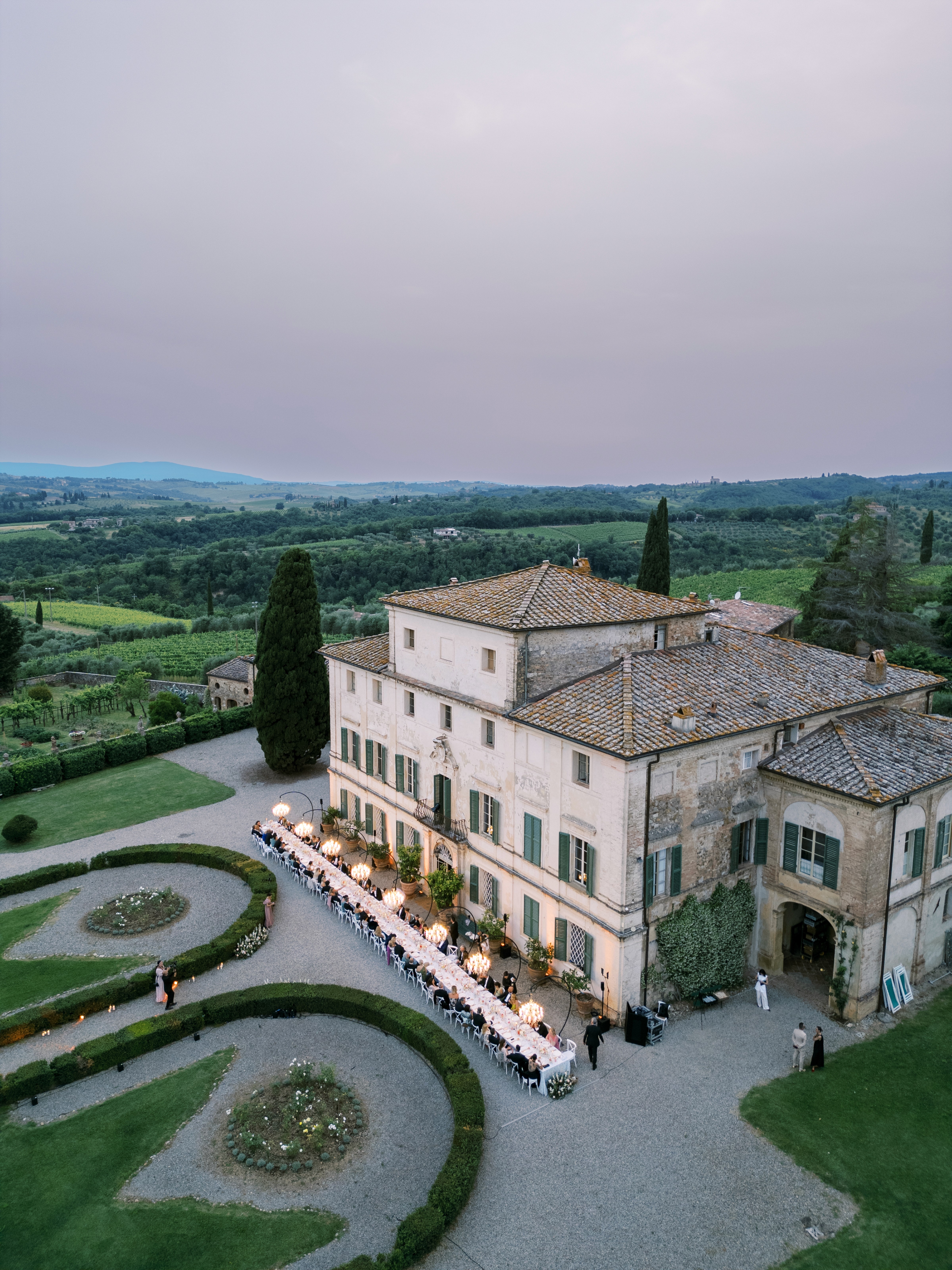 Tavolo imperiale apparecchiato al tramonto per matrimonio con catering di lusso, allestito davanti a una villa storica nelle colline toscane.