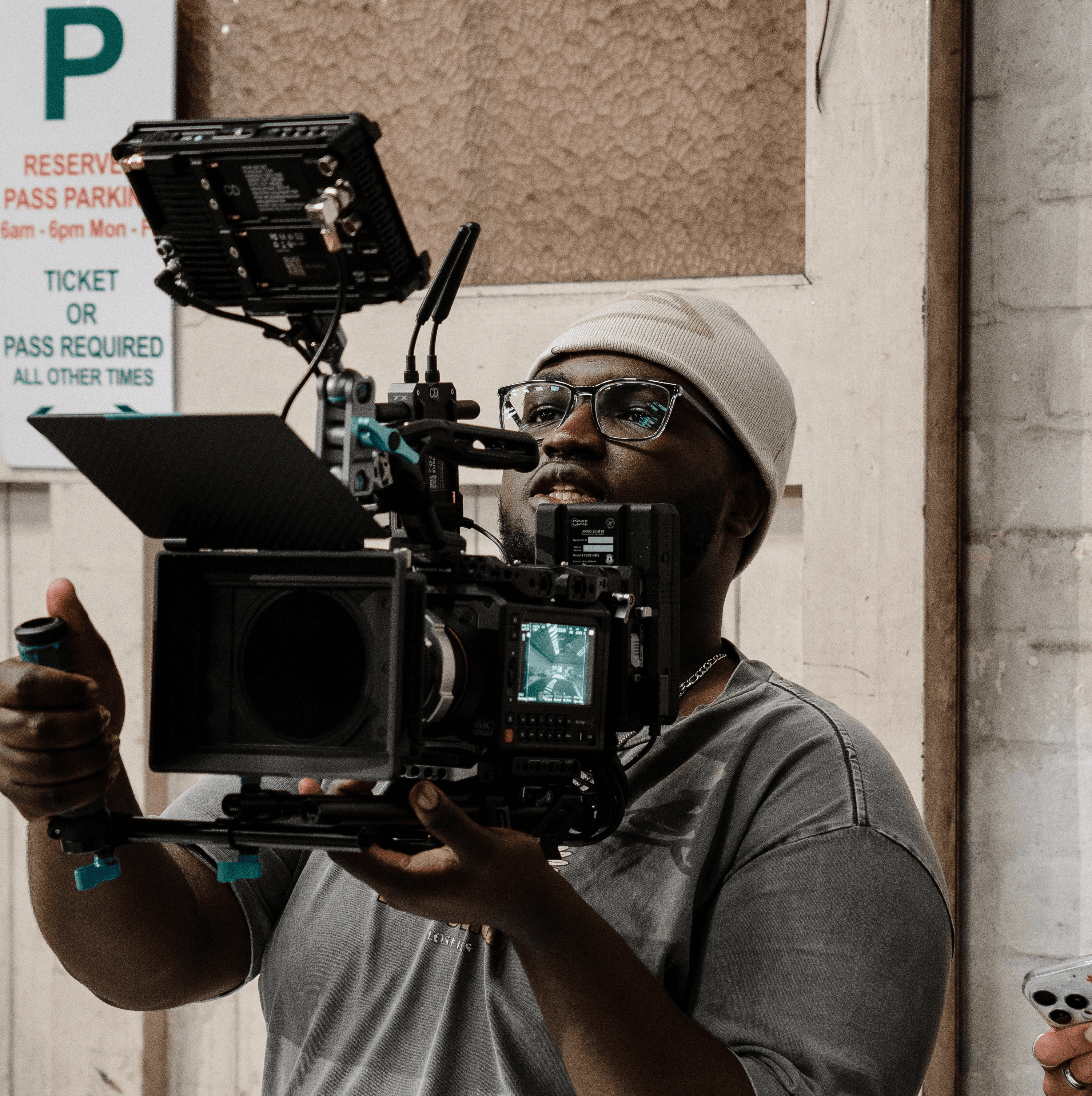 Young person with short hair wearing a dark flat cap, black cardigan, and white turtleneck, exuding a calm and composed expression against a plain background.