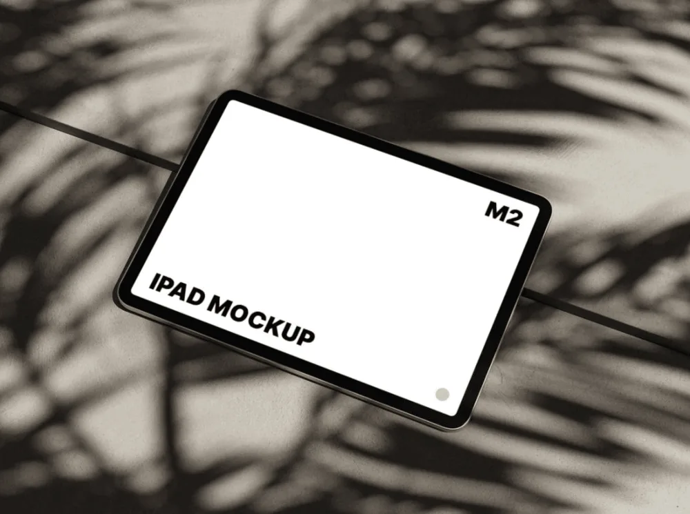 Mockup of an iPad M2 with a blank white screen, placed on a surface with soft palm leaf shadows. The device is angled slightly, creating a natural and aesthetic composition.