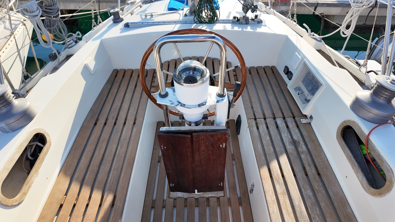 Contest 38 Ketch cockpit helm station — varnished teak slatted cockpit sole, large mahogany steering wheel with stainless steel pedestal, dome binnacle compass, genoa sheet winches, and teak companionway hatch boards