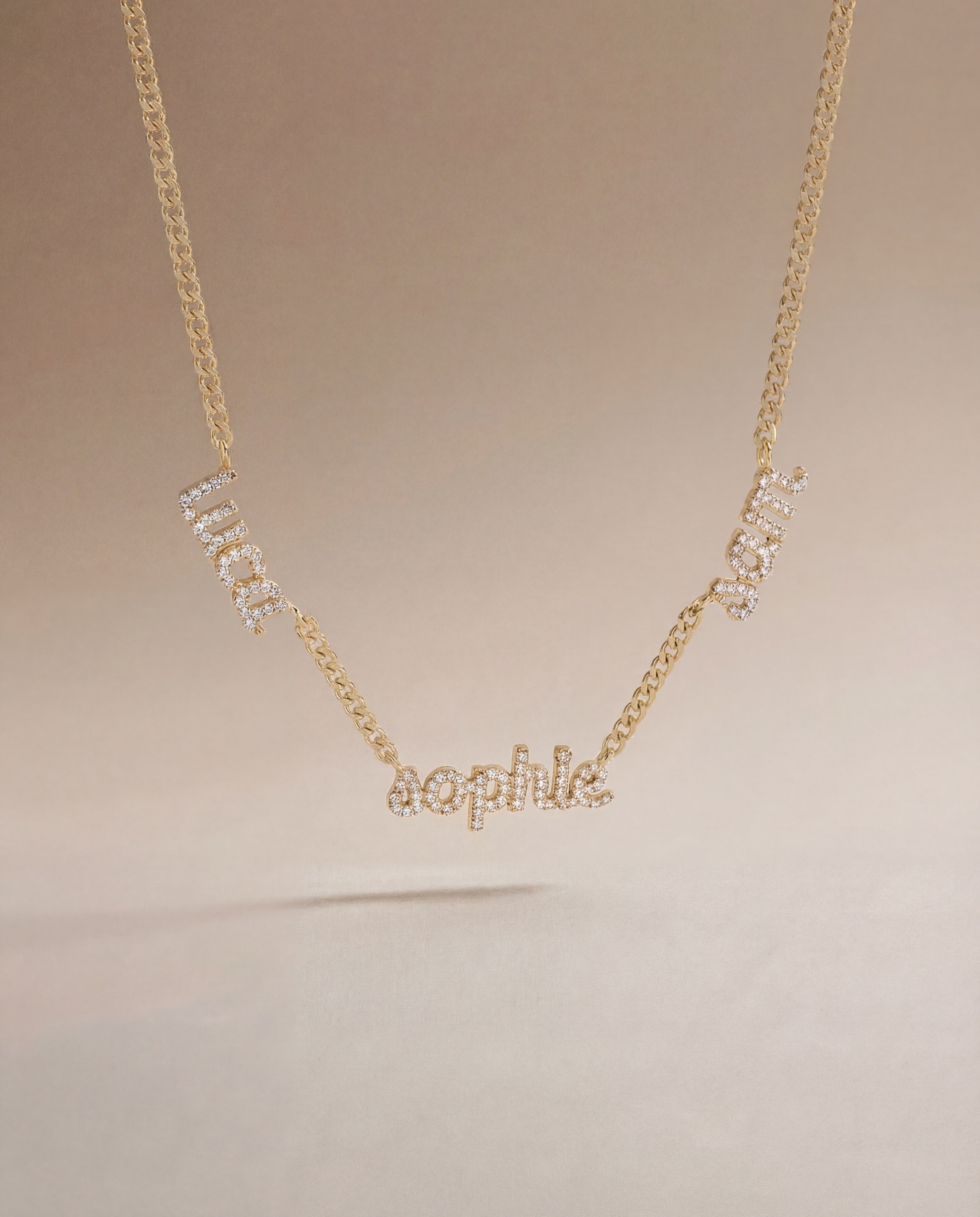 Vedder & Vedder — Gold name necklace suspended against a warm gradient.