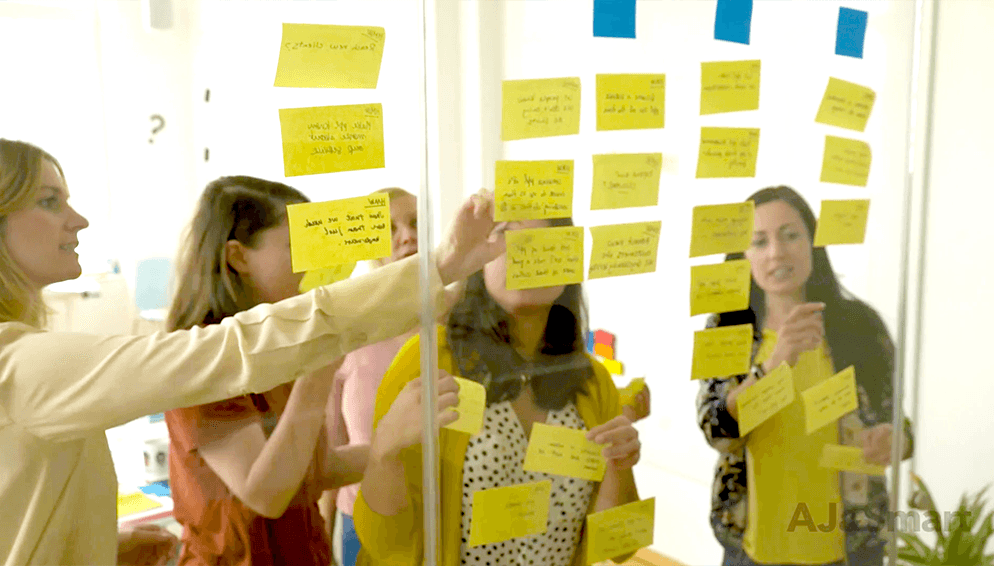 Workshop participants voting on sticky notes displayed on a glass board with dot voting