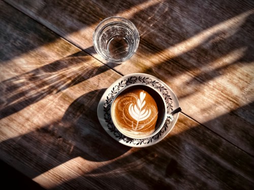 A flat white with latte art on a sunlit wooden table