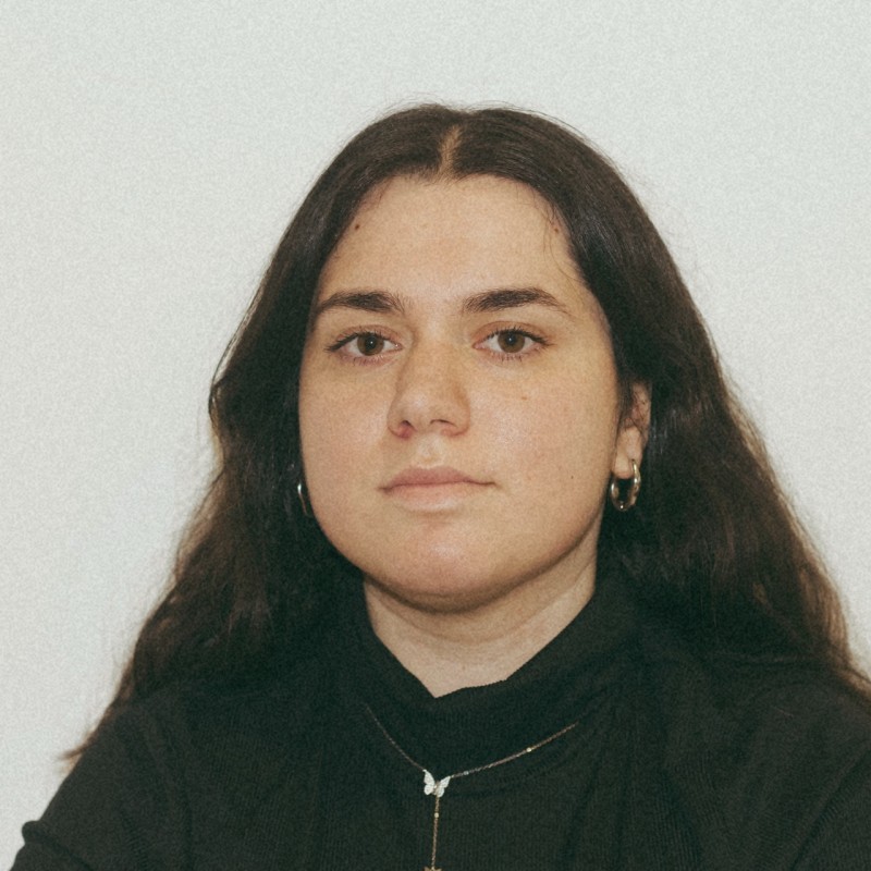 A thoughtful young person with dark hair gazes to the side, captured in soft black and white lighting.