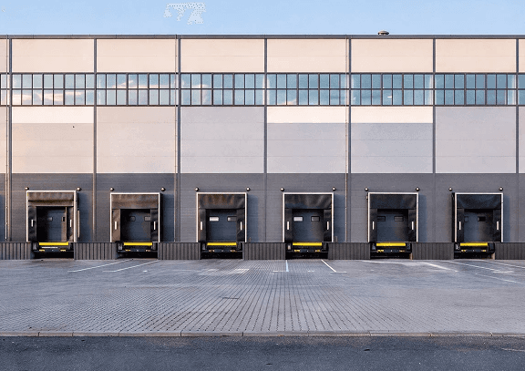 Row of industrial sectional garage doors at a large warehouse loading dock. Featuring heavy-duty commercial door systems with dock seals and levelers for logistics and distribution facilities.