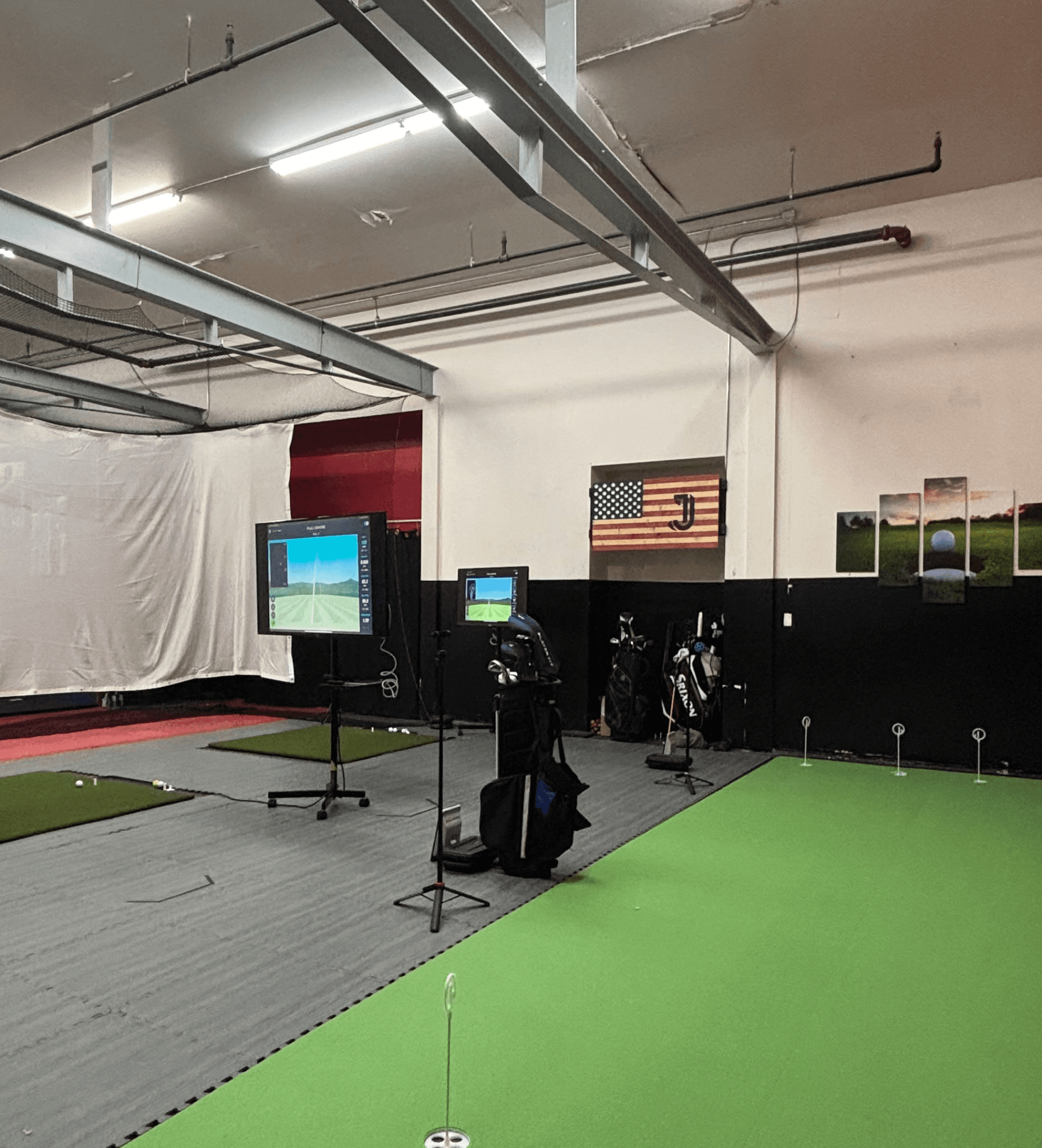 Monitors with golf simulations and golf bags next to a simulated green at an indoor facility.