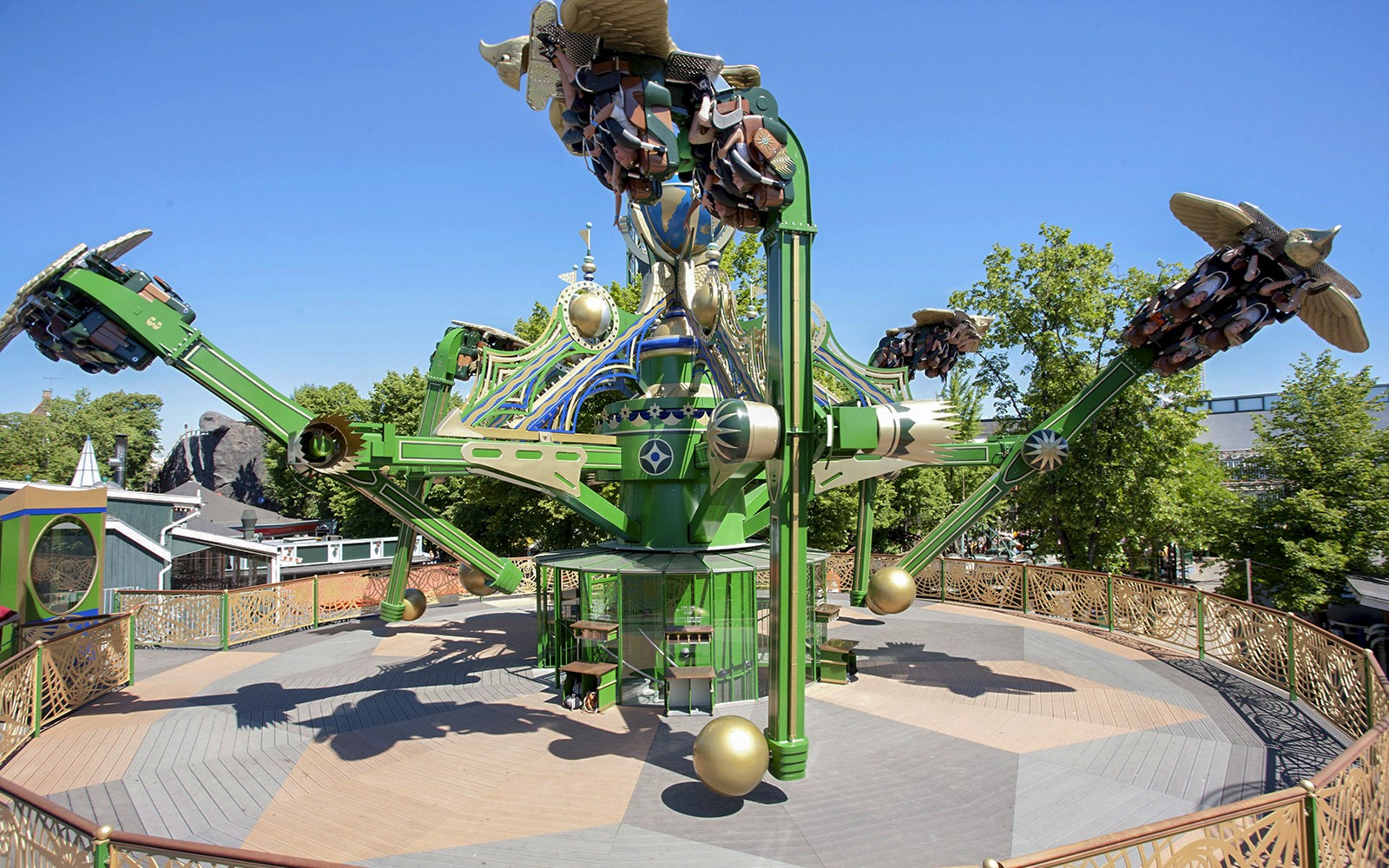 Aquila utazás a Tivoli Kertben, ahol az utasok forgó karokon ülnek a tiszta égbolt alatt.