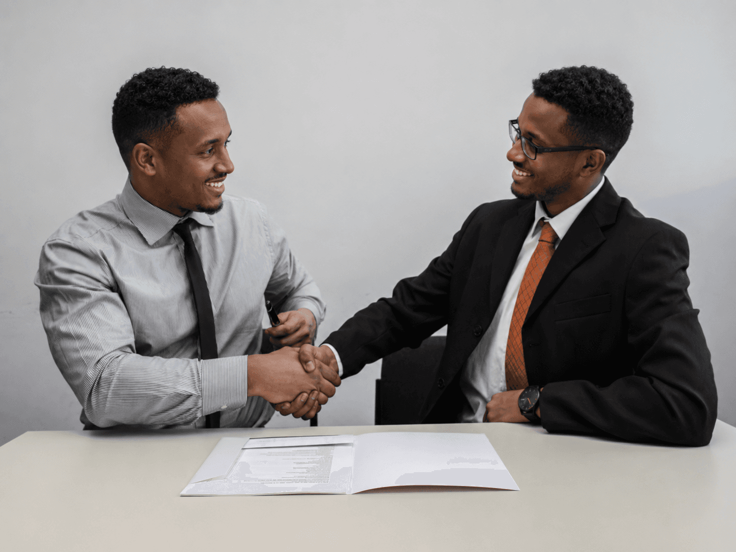 two men facing each other while shake hands and smiling