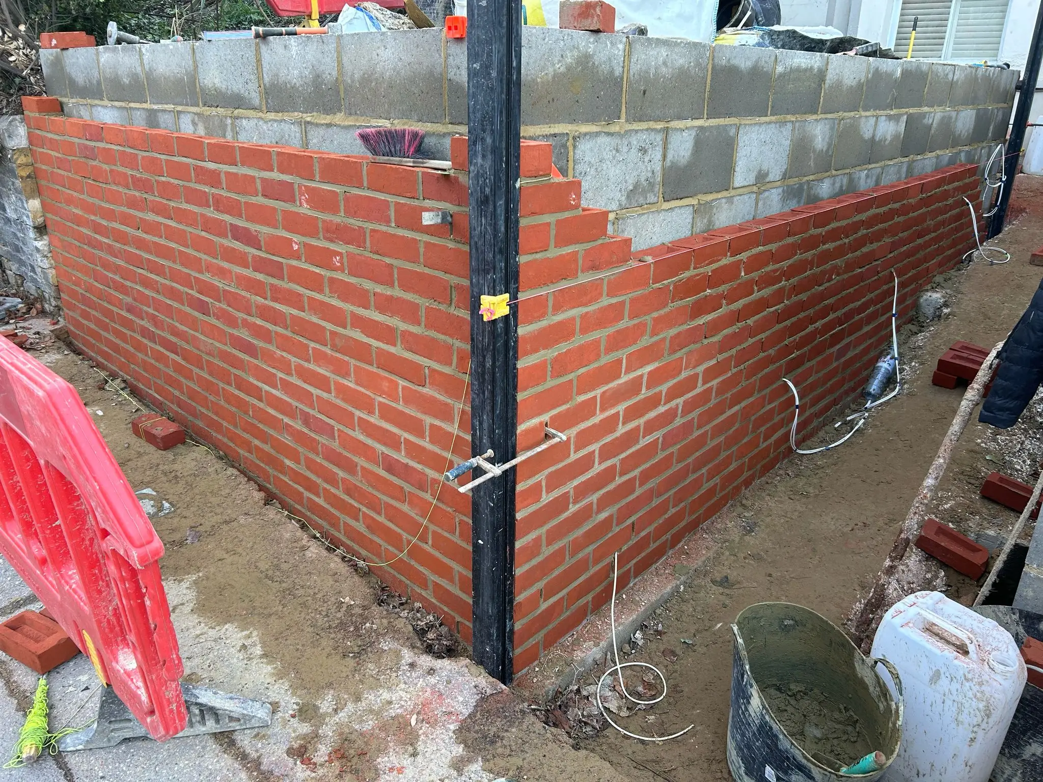 A corner view of a brick wall construction site, with tools and materials visible on the ground.