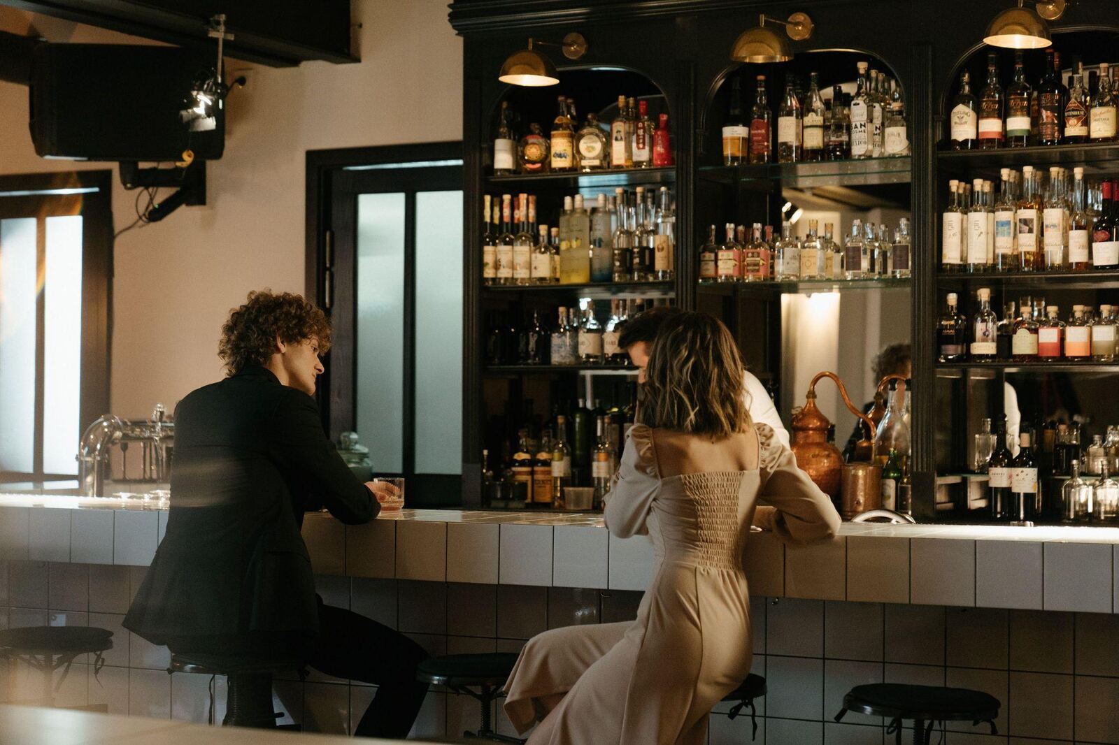 Ein Paar sitzt sich an einer Hotelbar nah gegenüber, im Hintergrund beleuchtete Regale mit Spirituosen