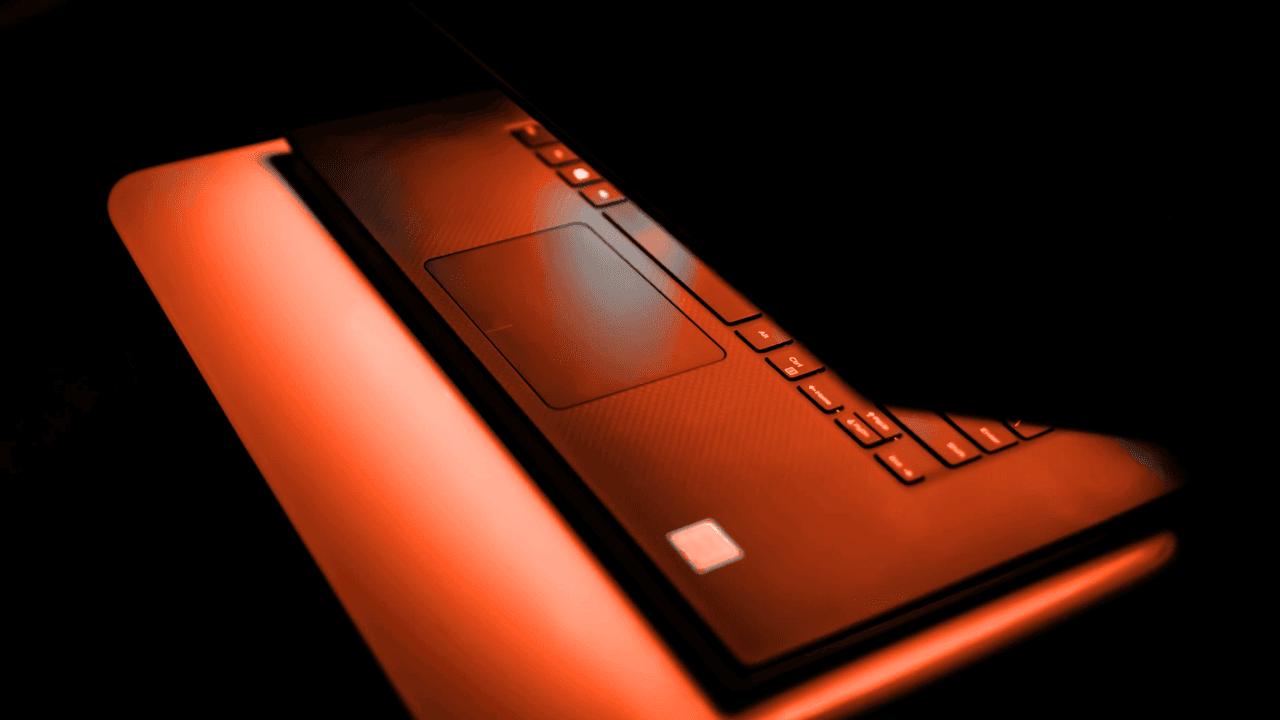 Close-up of a sleek black laptop with orange illuminated keys against a dark background.
