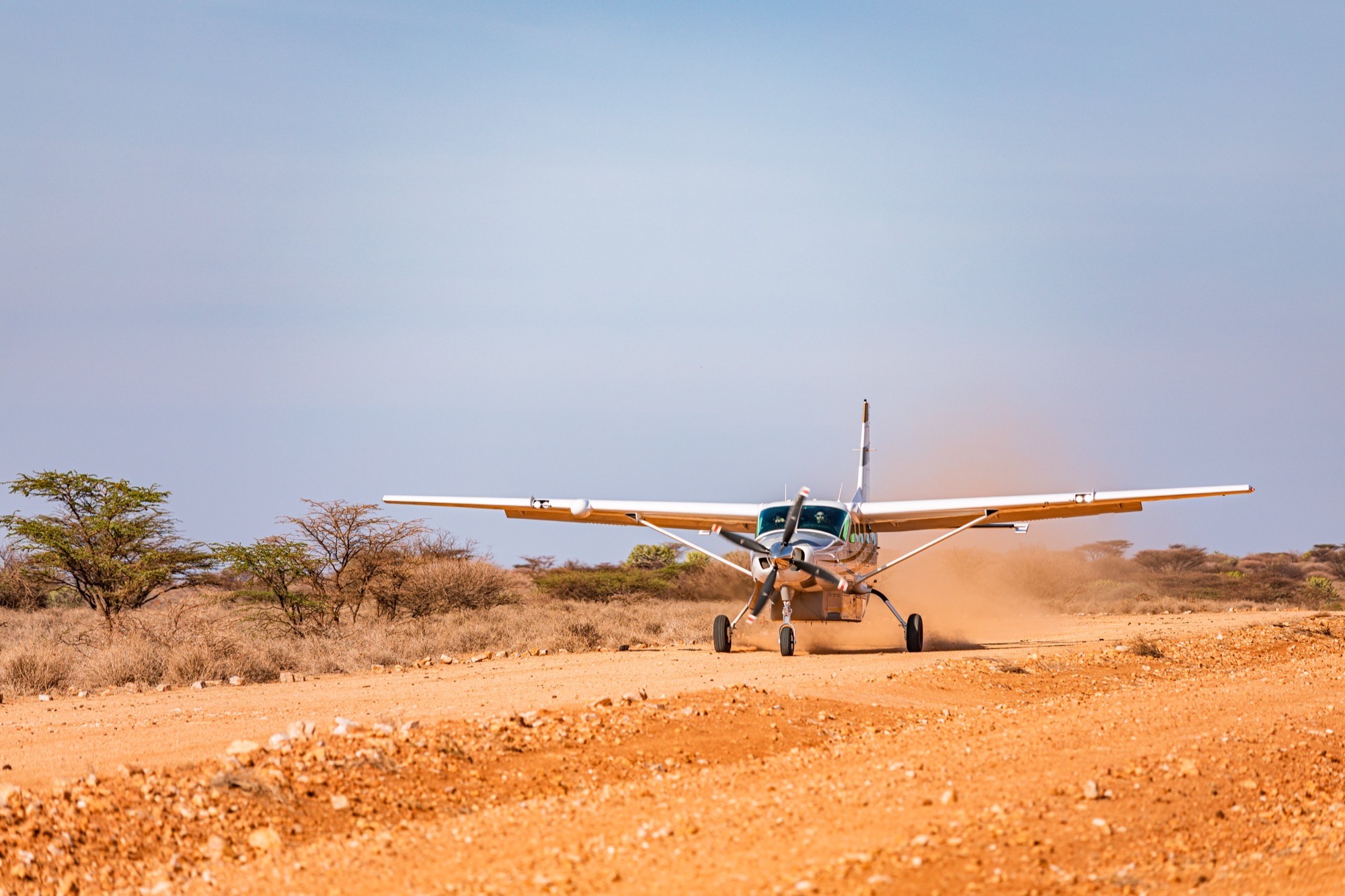 A light aircraft landing on a remote bush airstrip, dust rising behind it