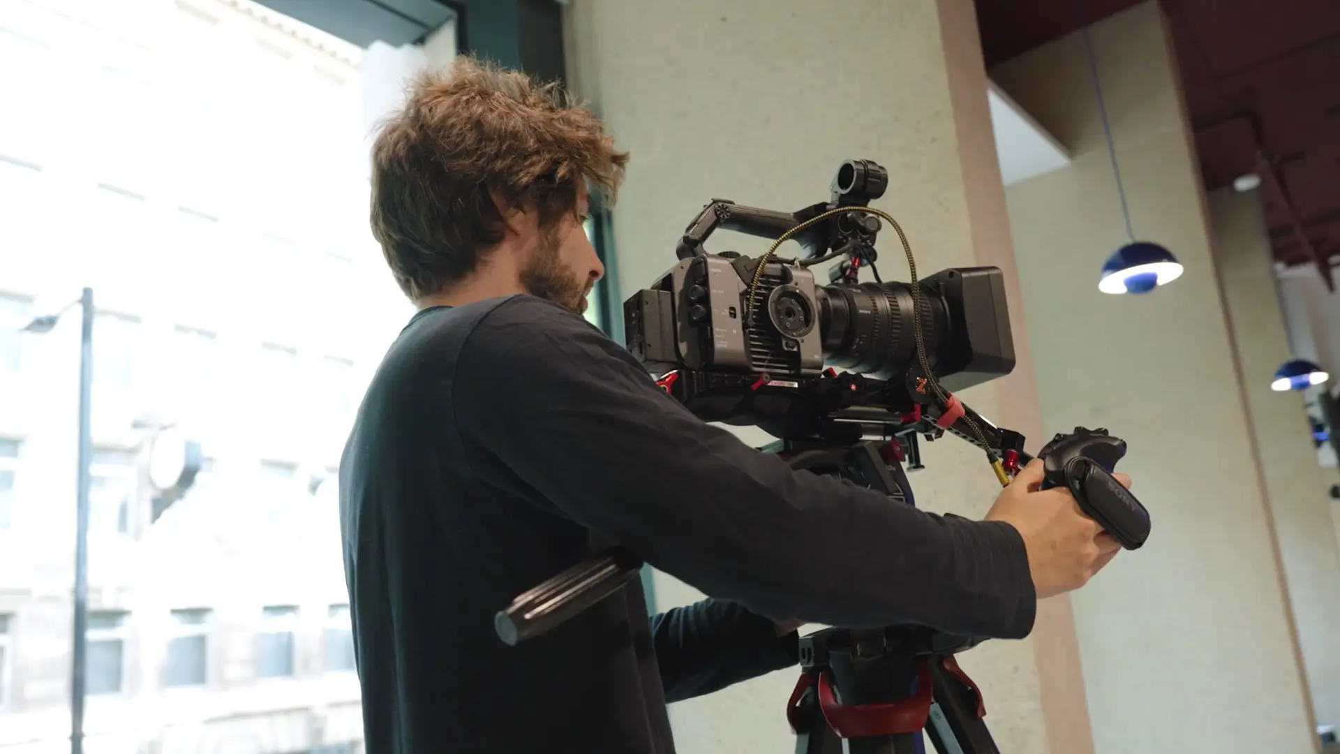 Camera operator filming event content using a broadcast camera on a tripod.