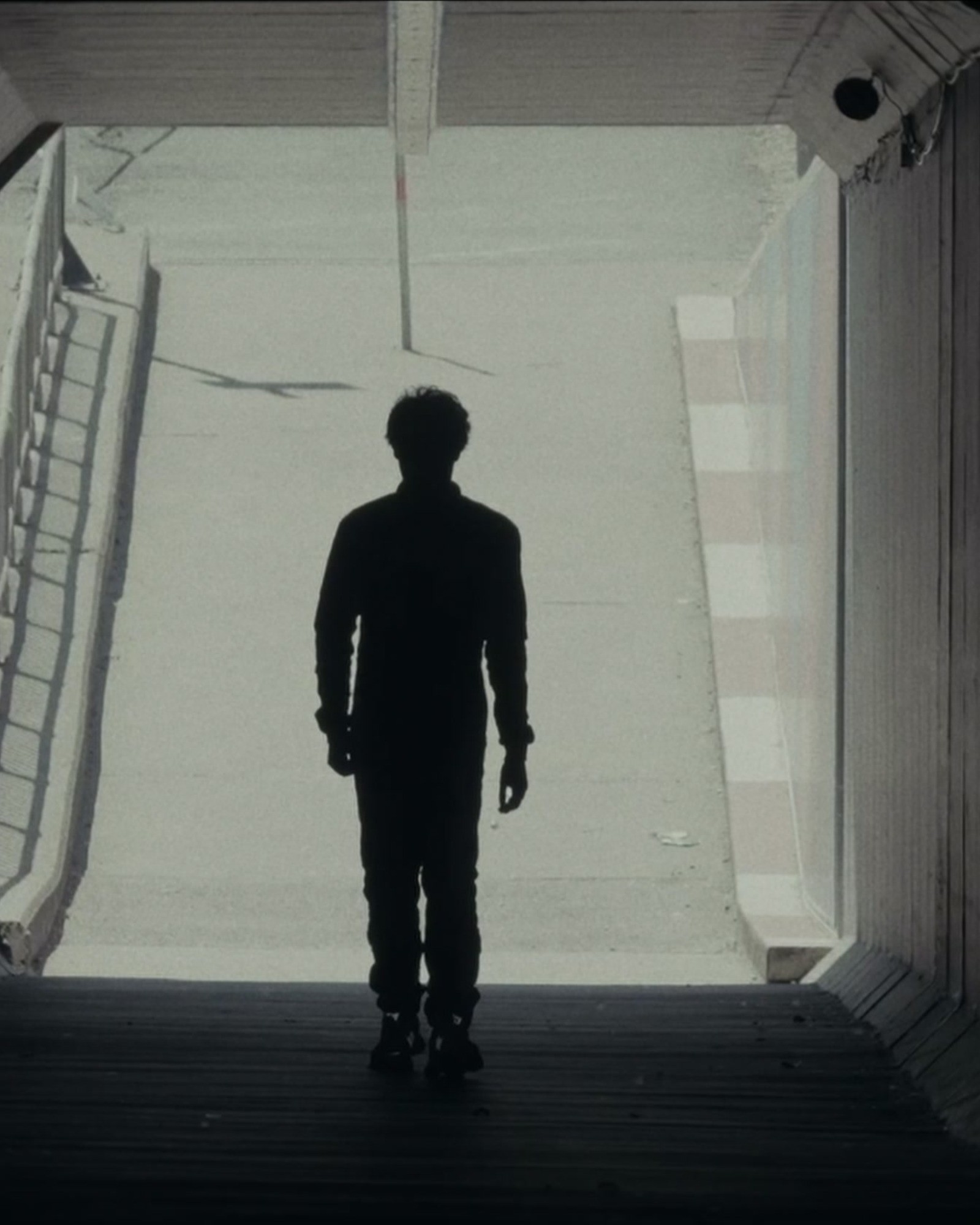 A silhouetted figure standing in a bright doorway at the end of a dark tunnel