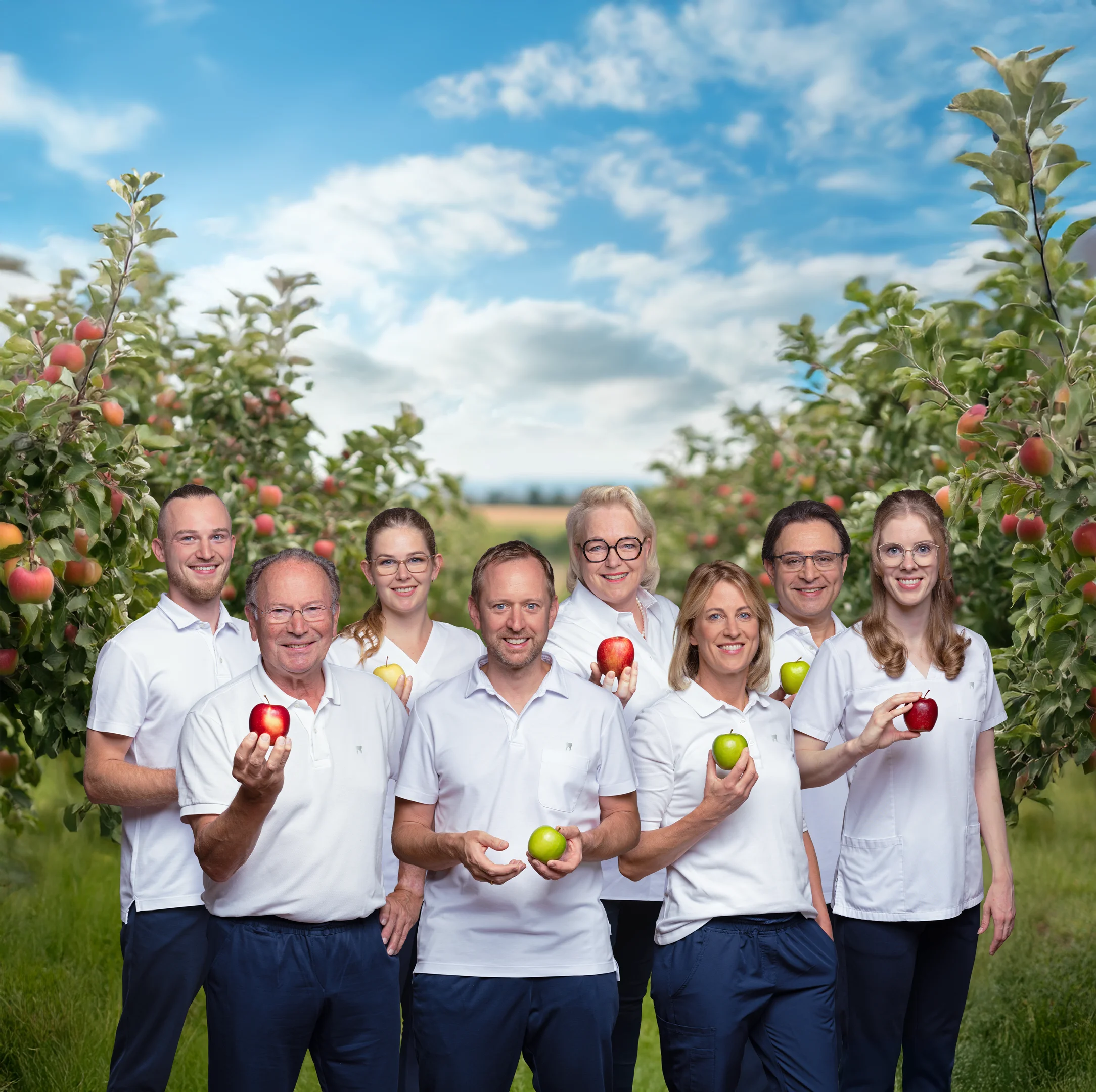Gruppenfoto des Zahnarzt-Teams in einem Feld mit Apfelbäumen