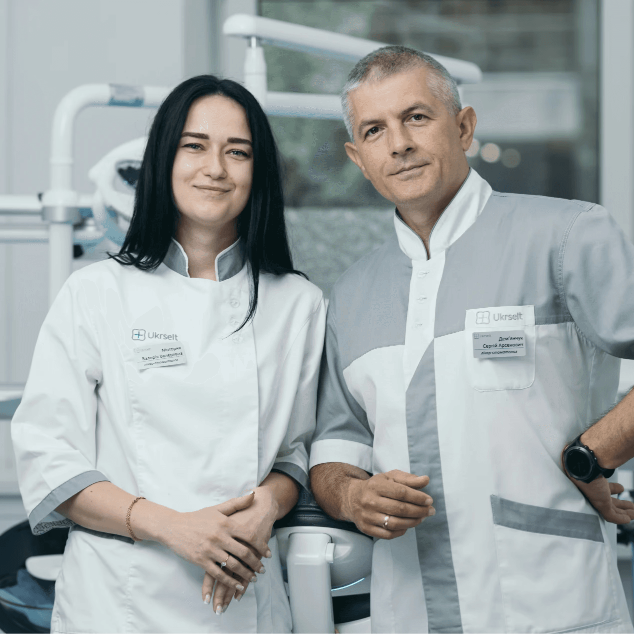 Two dentists are standing in the dental office, smiling, ready to receive patients.