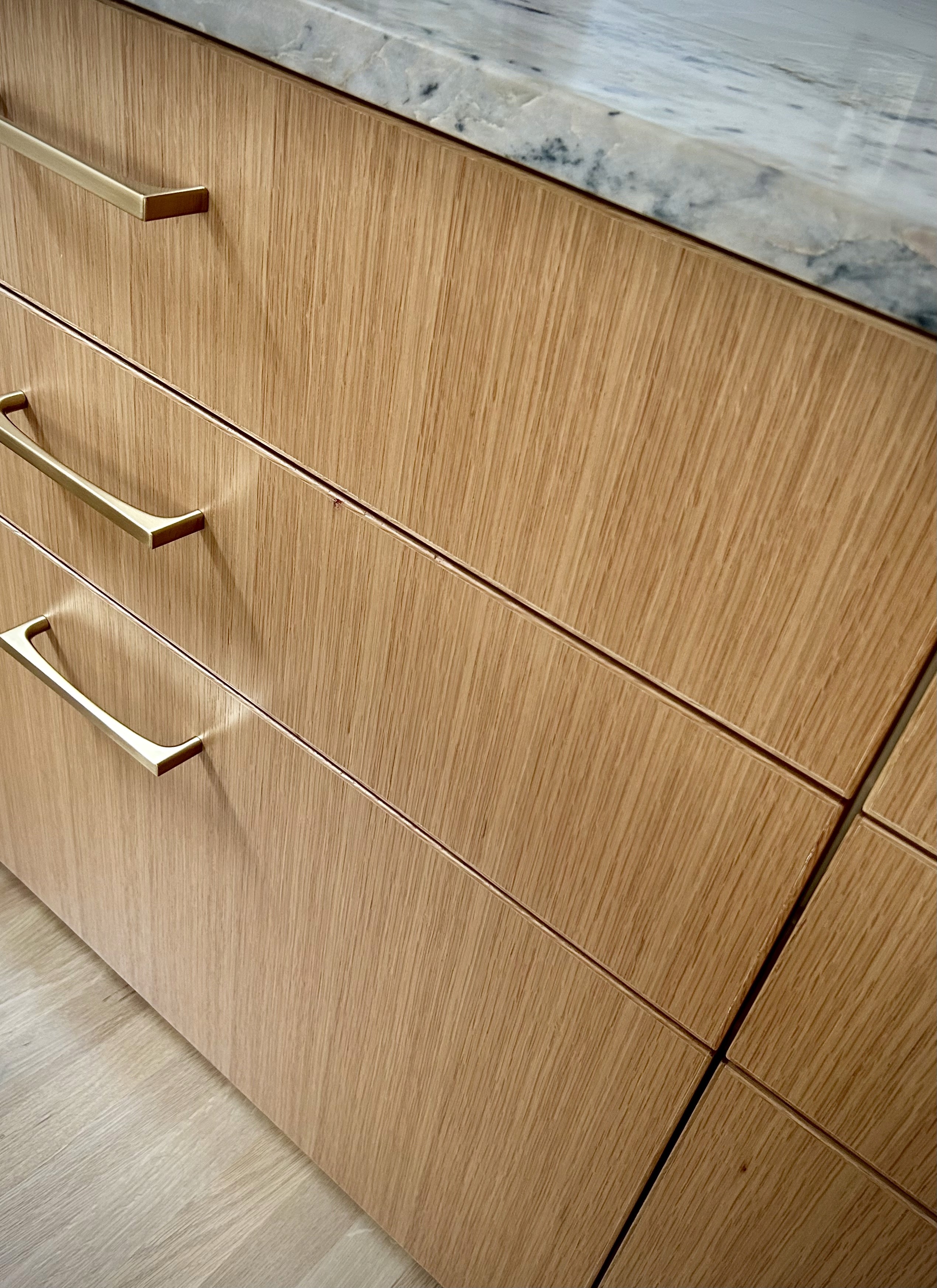 A detail of white oak cabinet drawers and brass hardware.