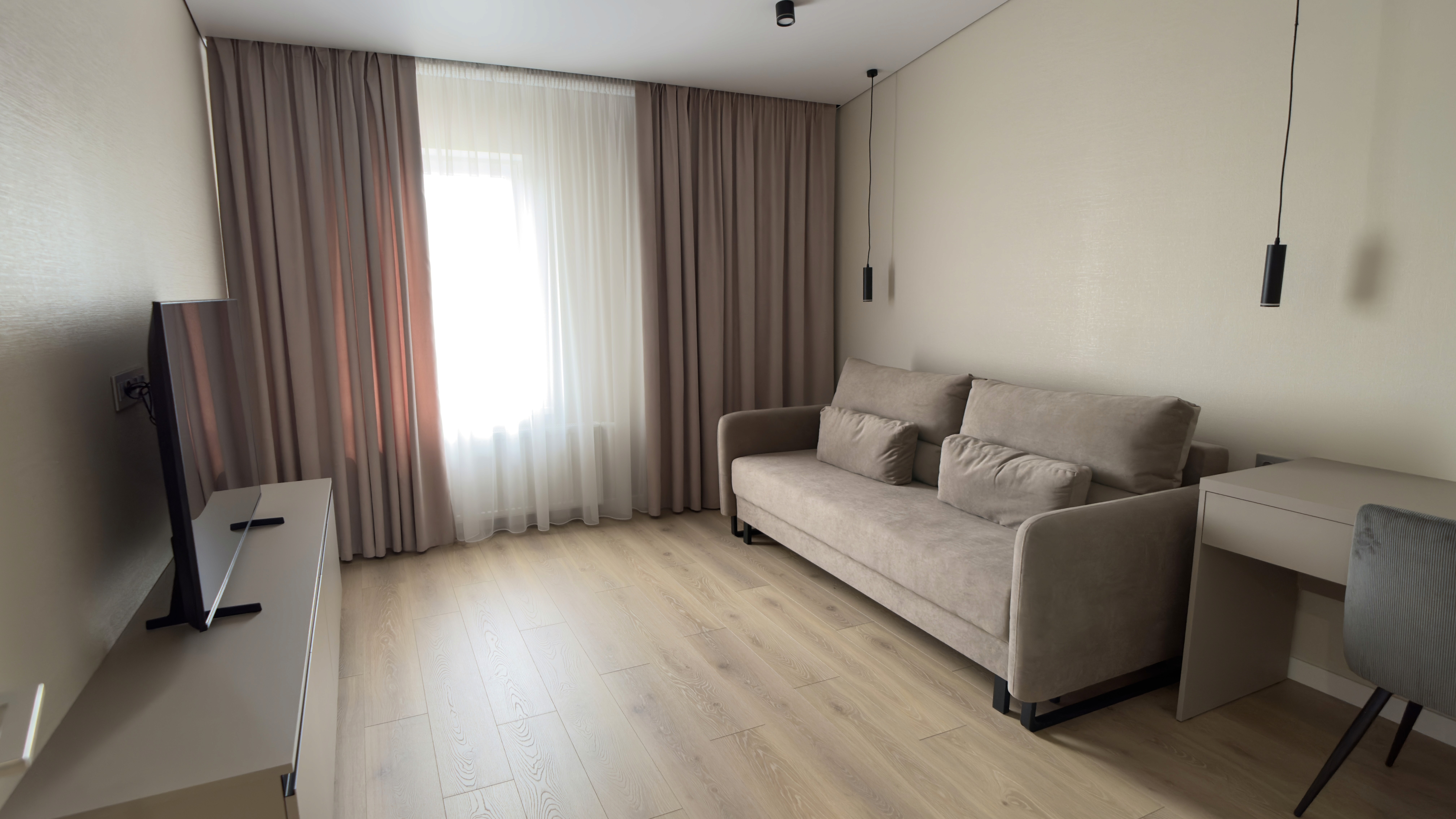 Вітальня з м’яким диваном, телевізором і письмовим столом біля вікна