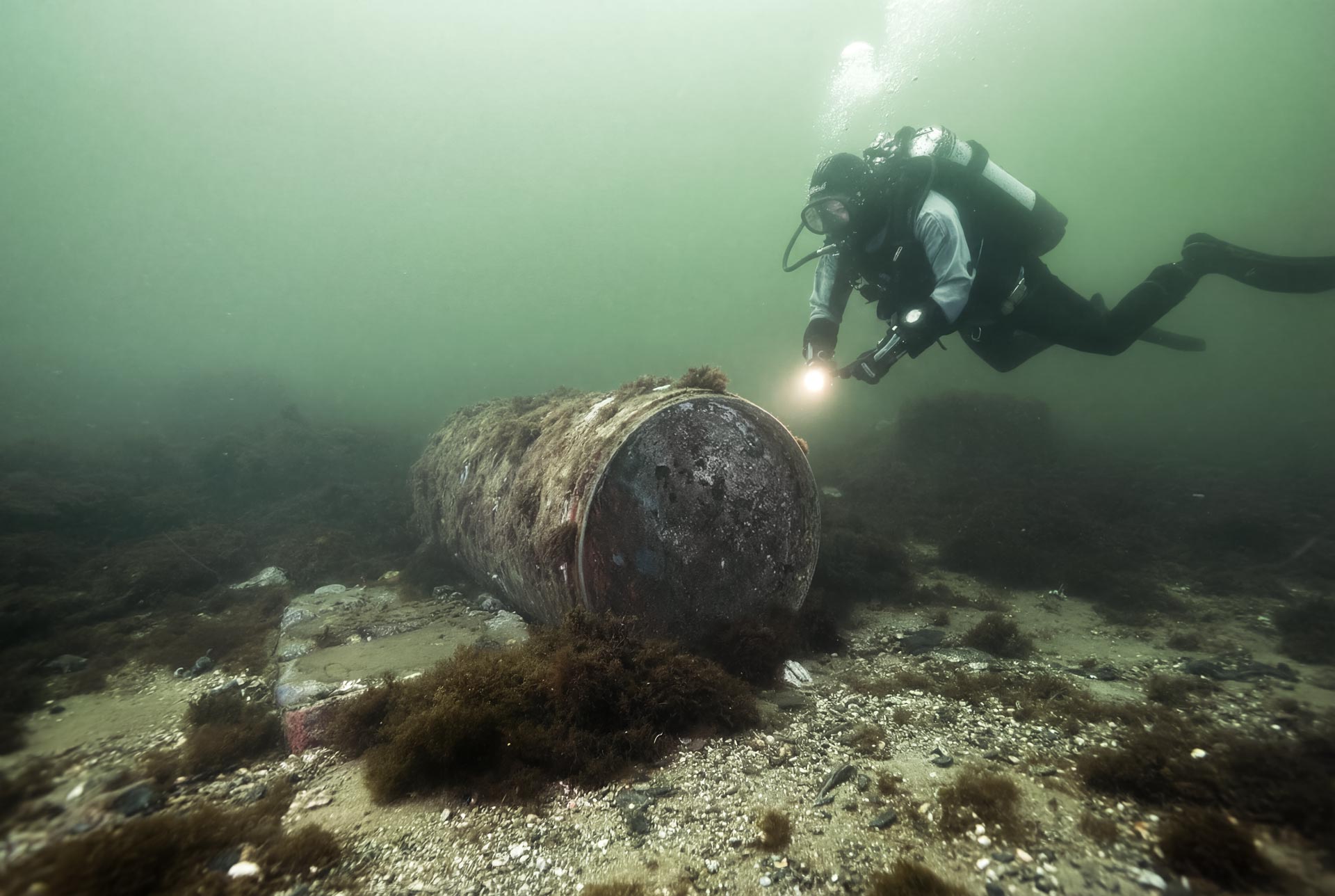 EOD diver inspecting a submerged unexploded bomb on the seabed during underwater clearance operations.
