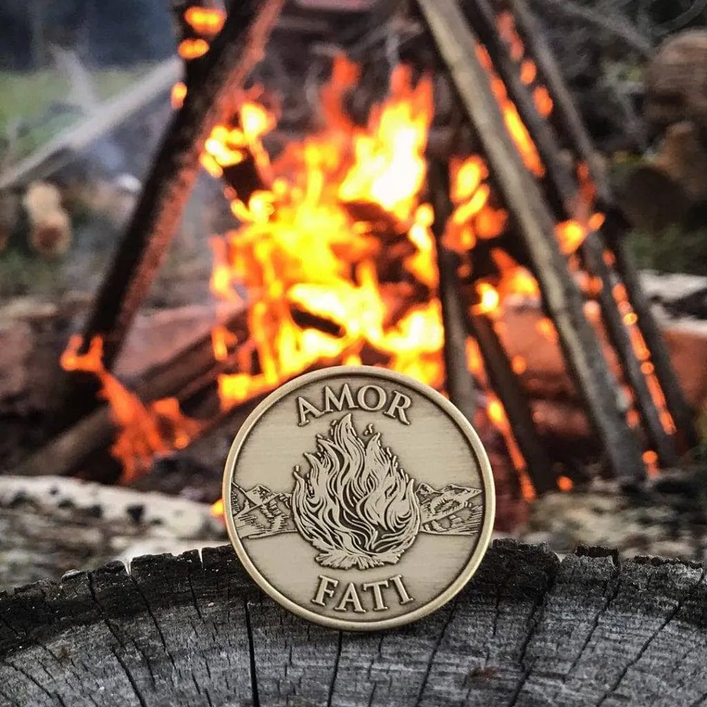 a coin with "amor fati" inscription and a burning fire design, in front of a campfire