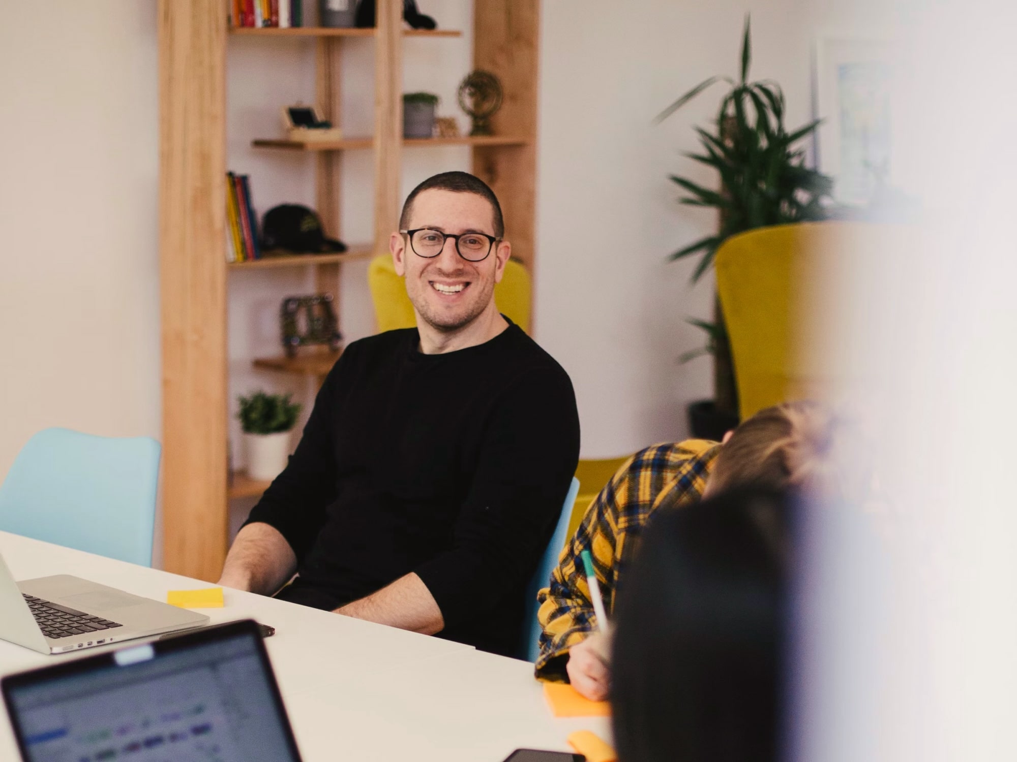 A cheerful man in glasses sits at a table with two laptops, thrilled to begin a project with GoDutch as his bank.