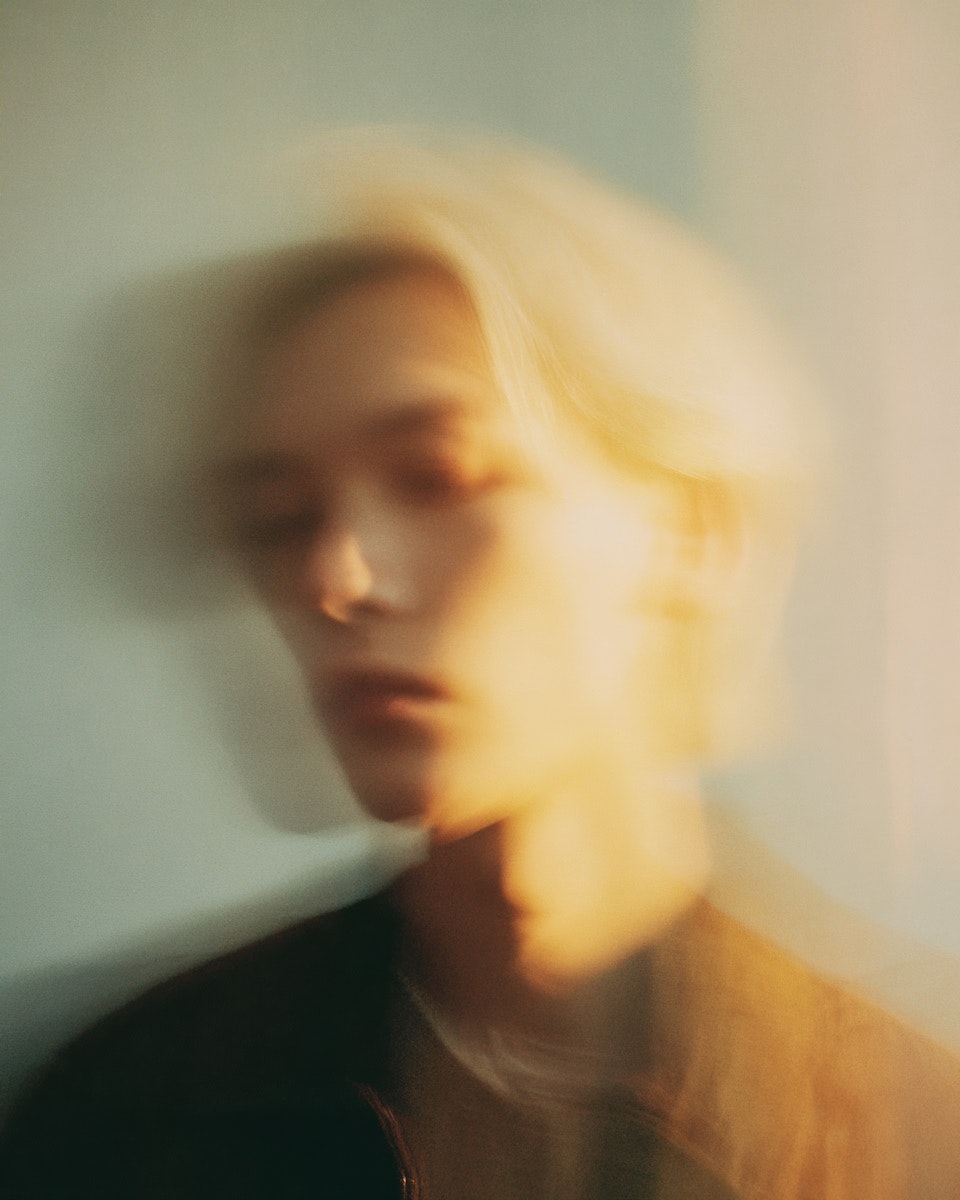 A blurred portrait of a person with light blond hair, creating an ethereal and soft visual effect.