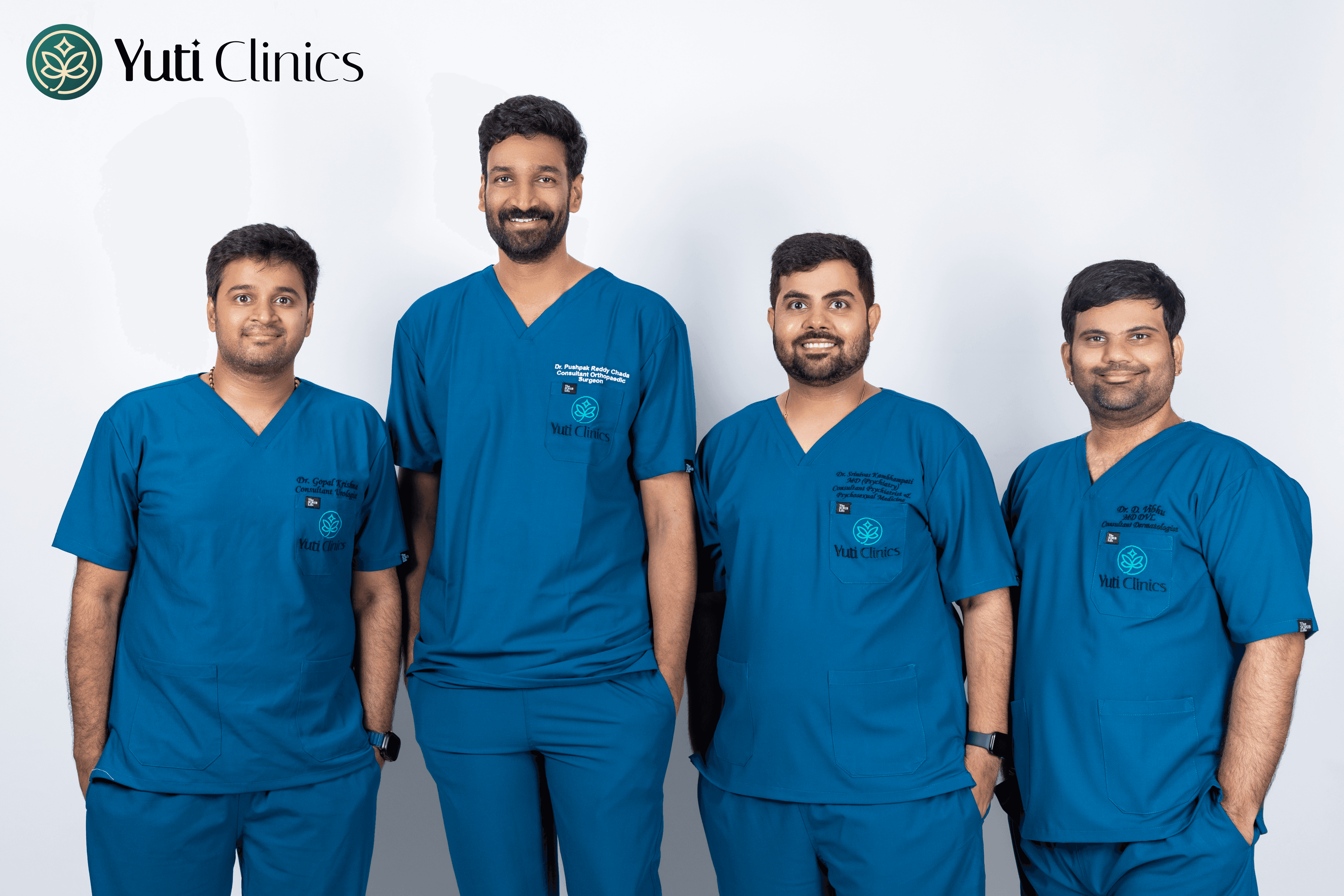 A young person with curly hair smiles at the camera while sitting in front of a laptop against a dark background.