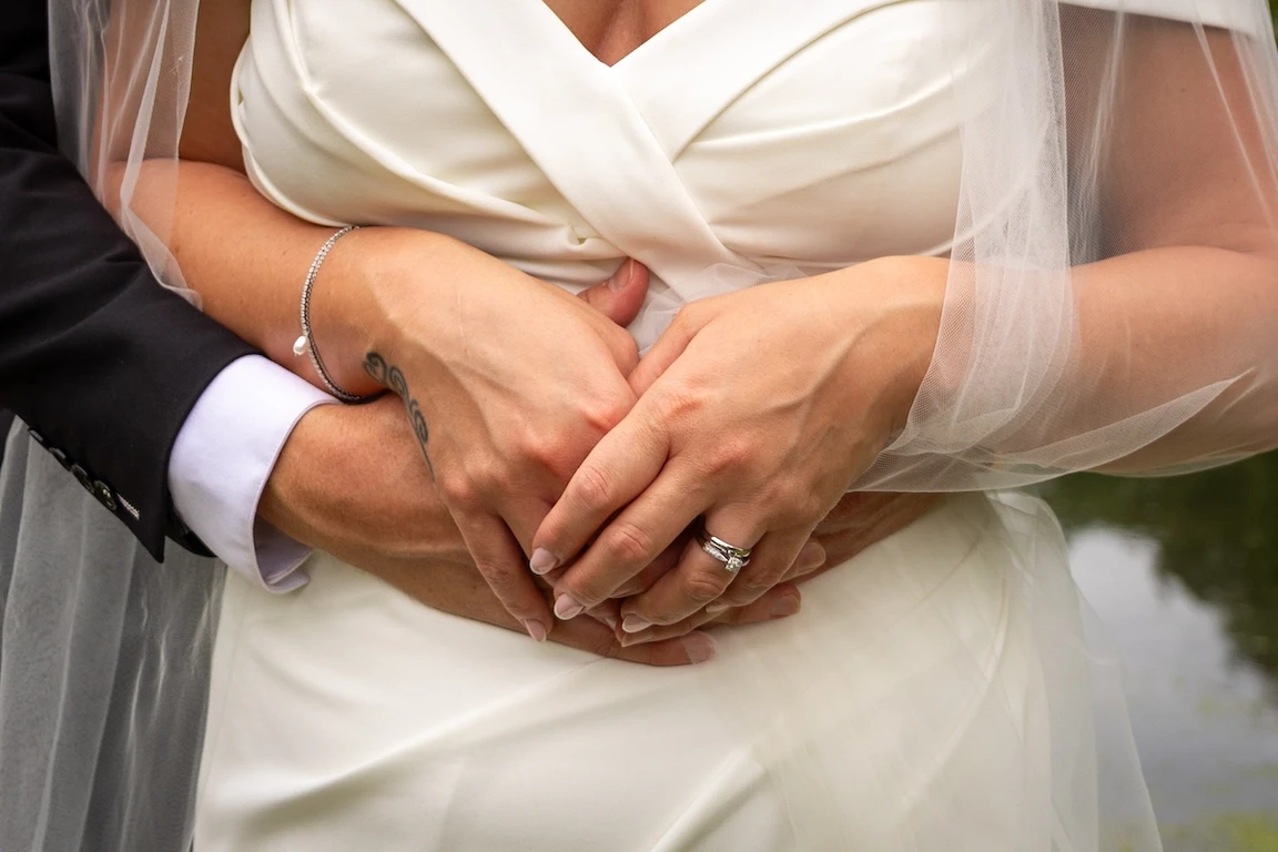 Close-up of bride and groom holding hands showing wedding rings