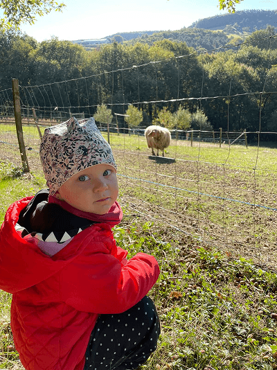 Holčička v červené bundě sedící v trávě na zahradě