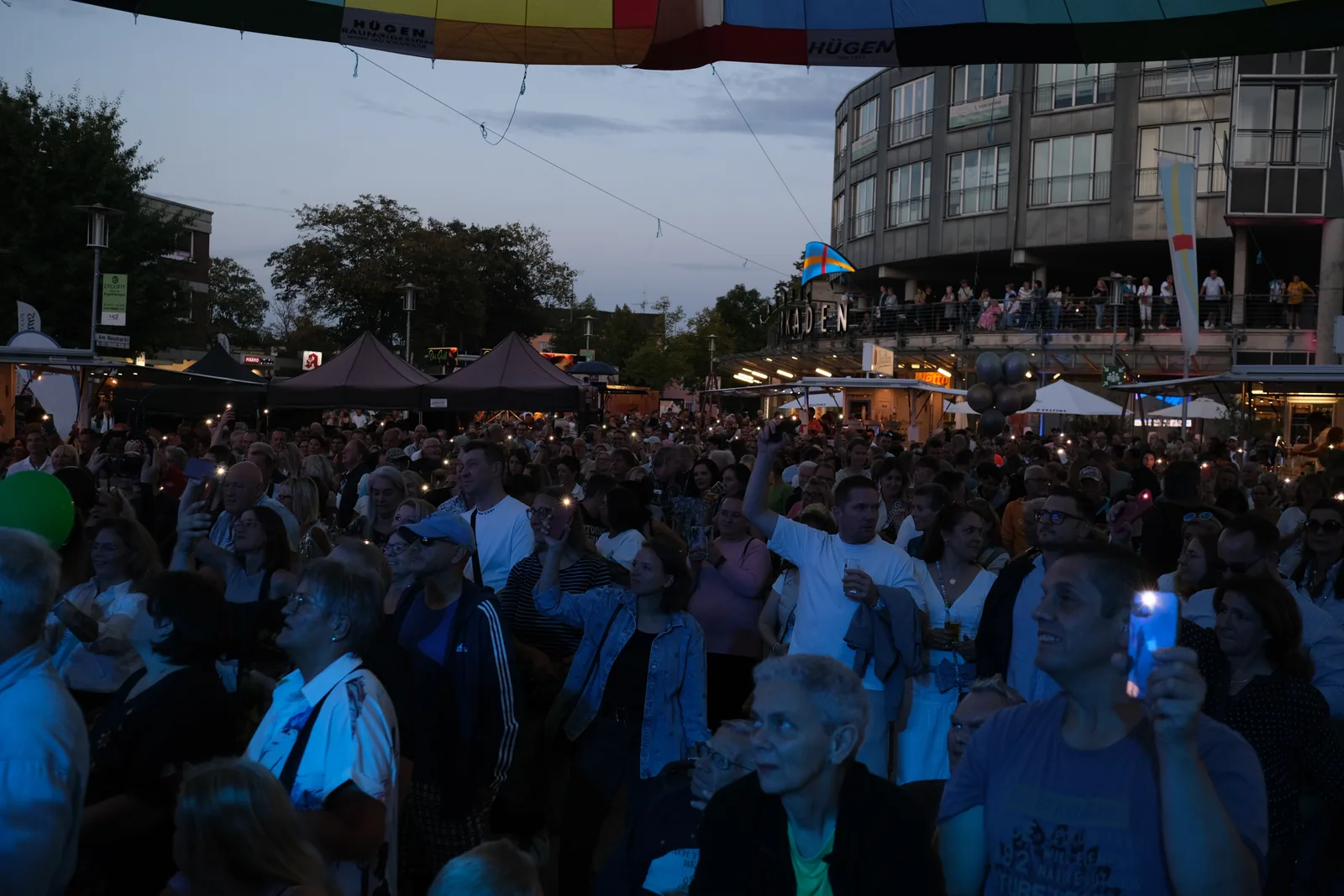 Publikum vor der Bühne in der Dämmerung, dahinter die Häuser der Stadtmitte.