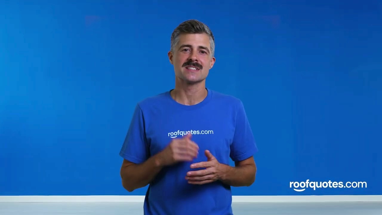 Man with a mustache wearing a blue t-shirt with the Roofquotes.com logo in front of a blue background.